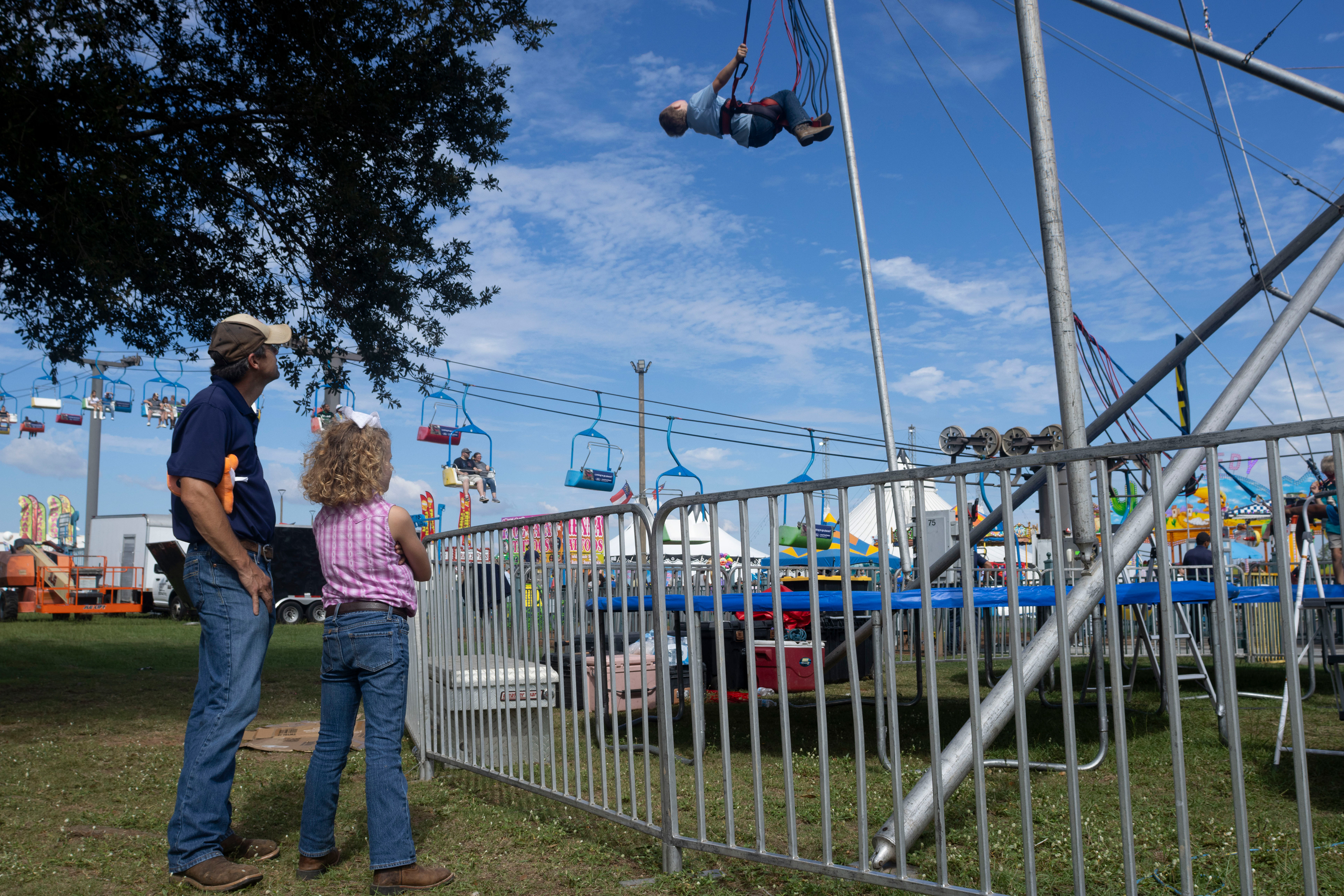 Rahn Milligan stands with his daughter, Olivia Milligan, 8, as they watch William Milligan, 6, jump on a trampoline at the Georgia National Fairgrounds and Agriculture Center on Oct. 5, 2024. This is Olivia's fourth year showing livestock at the fair, continuing the tradition of her father, who has been showing animals at the Georgia National Fair since the 1990's. 