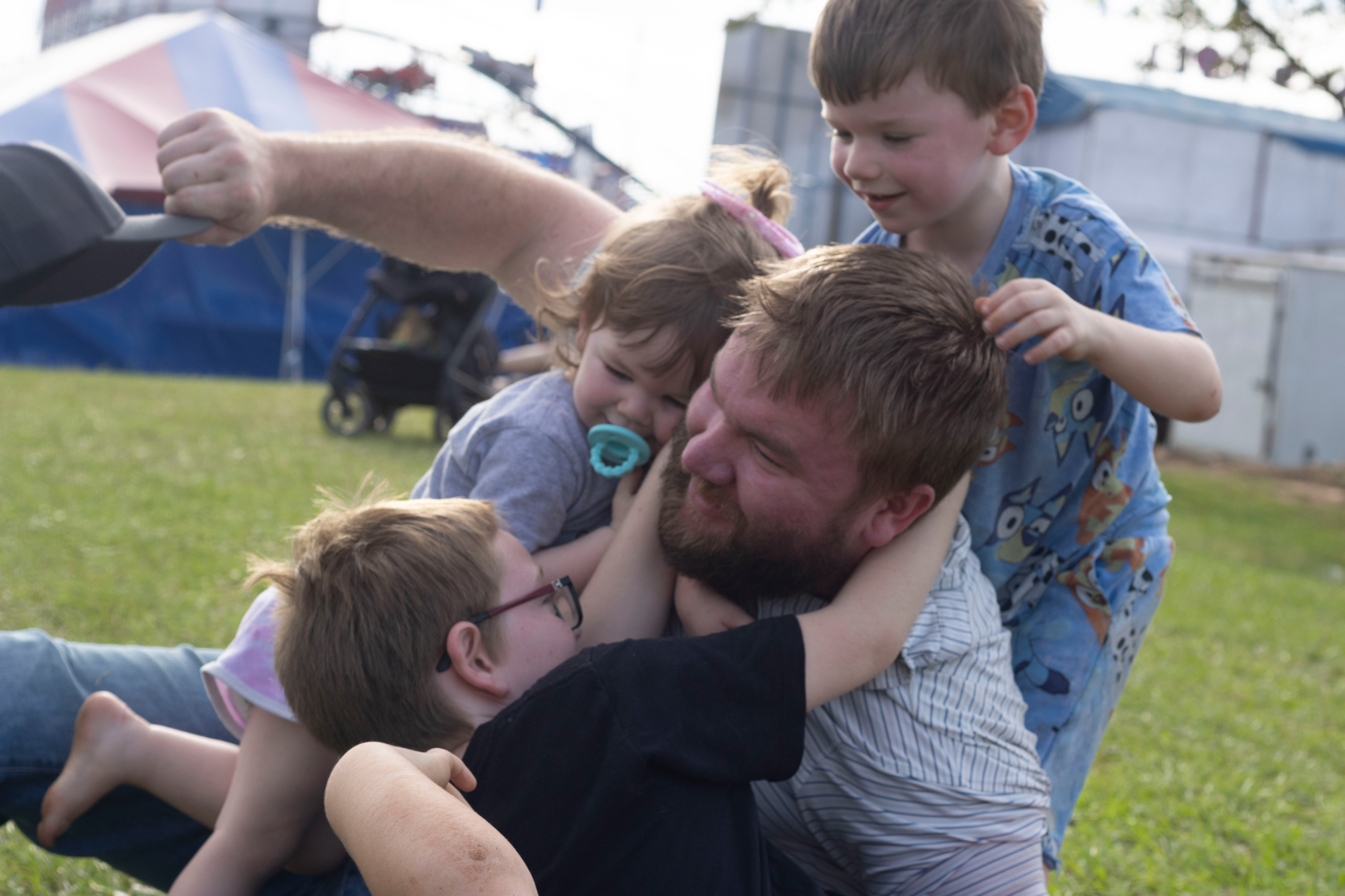 Matthew Pressley of Albany, Georgia, plays and wrestles with his children in the grass at the Georgia National Fairgrounds and Agriculture Center on Oct. 5, 2024.