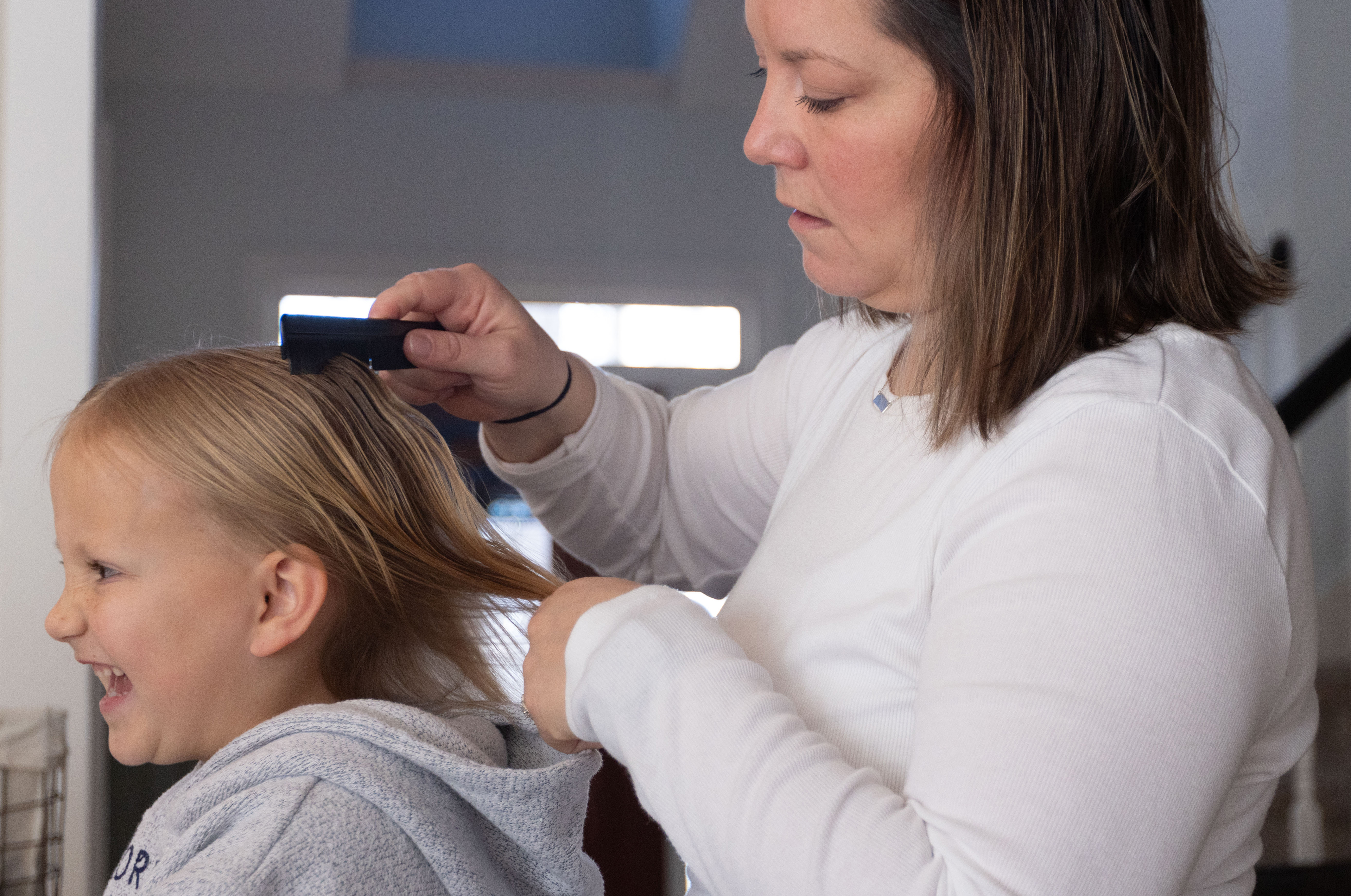 Jessica Adams combs the hair of her daugher, Mabel Adams (6), at their house in Monroe, Ga shortly before they leave to watch Theodore Adams (10) play baseball on Feb. 22, 2025. 