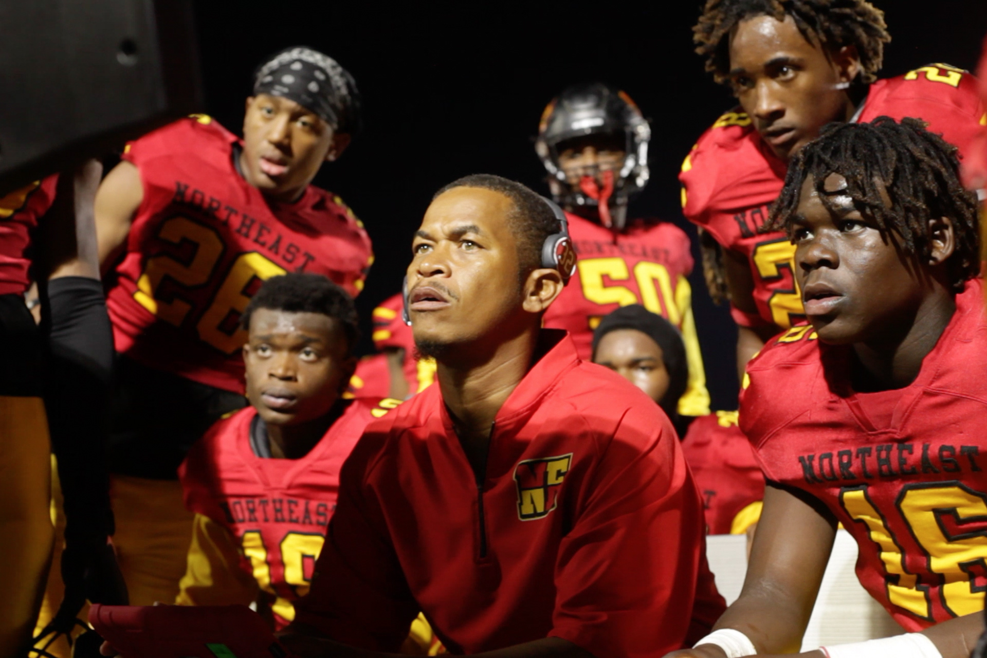 Northeast highschool football players and an assistant coach watch a screen that runs through their plays on the sidelines of Ed Defore Sports Complex on Oct. 7, 2022. It is Northeast's homecoming game, which they won 49-16.
