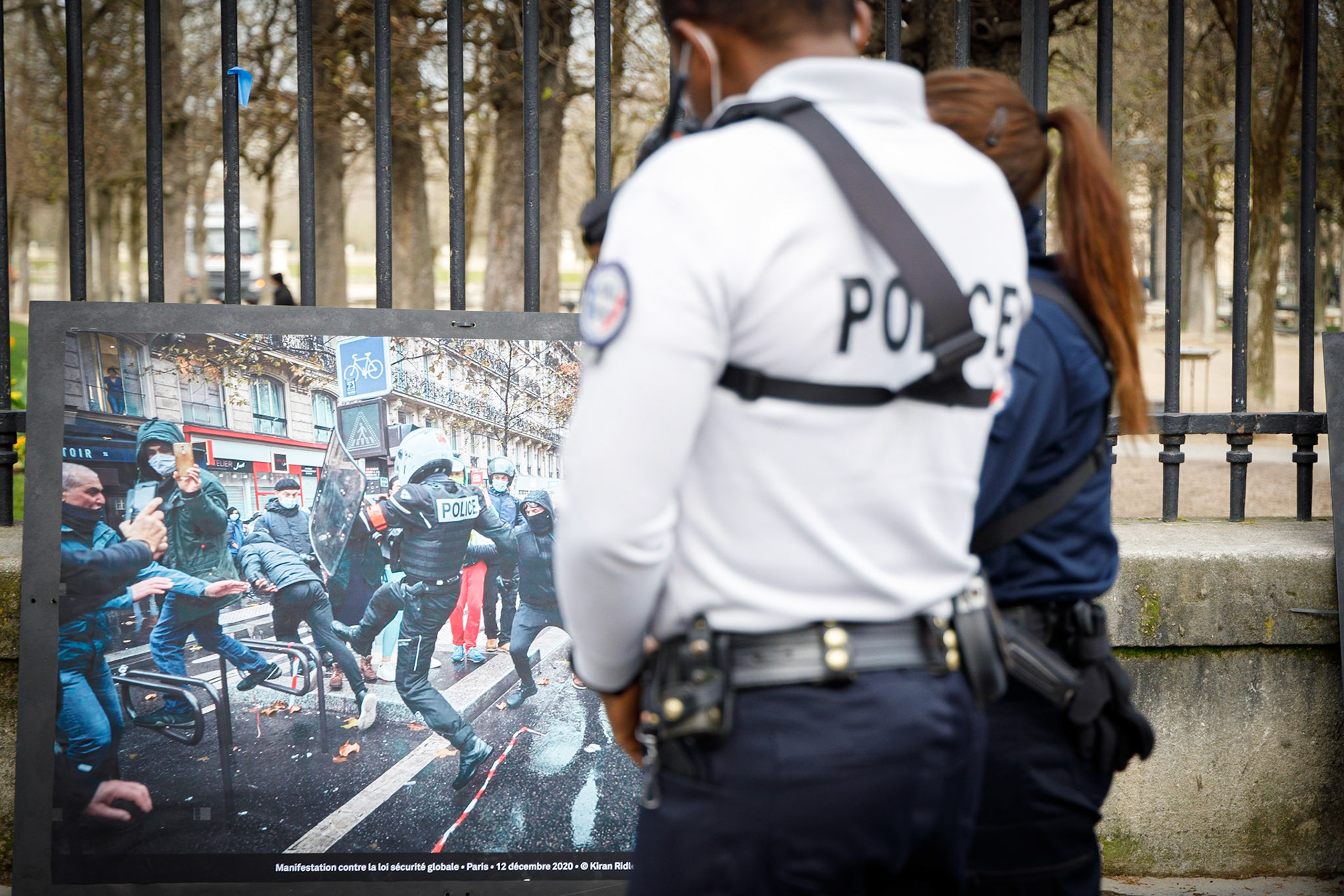 Des policiers devant une exposition de photos de violences policières installée sur les grilles du jardin du Luxembourg par des militants d' associations (Attac, la SRF, ...) membres de la coordination stop loi sécurité globale, le 18 mars 2012 à Paris. Cette action de désobéissance civile sous la forme de l'installation d'une exposition a pour but de dénoncer le projet de loi de sécurité globale et notamment son article 24 débattu au Sénat depuis le 16 mars.Paris, FRANCE - 18/03/2021