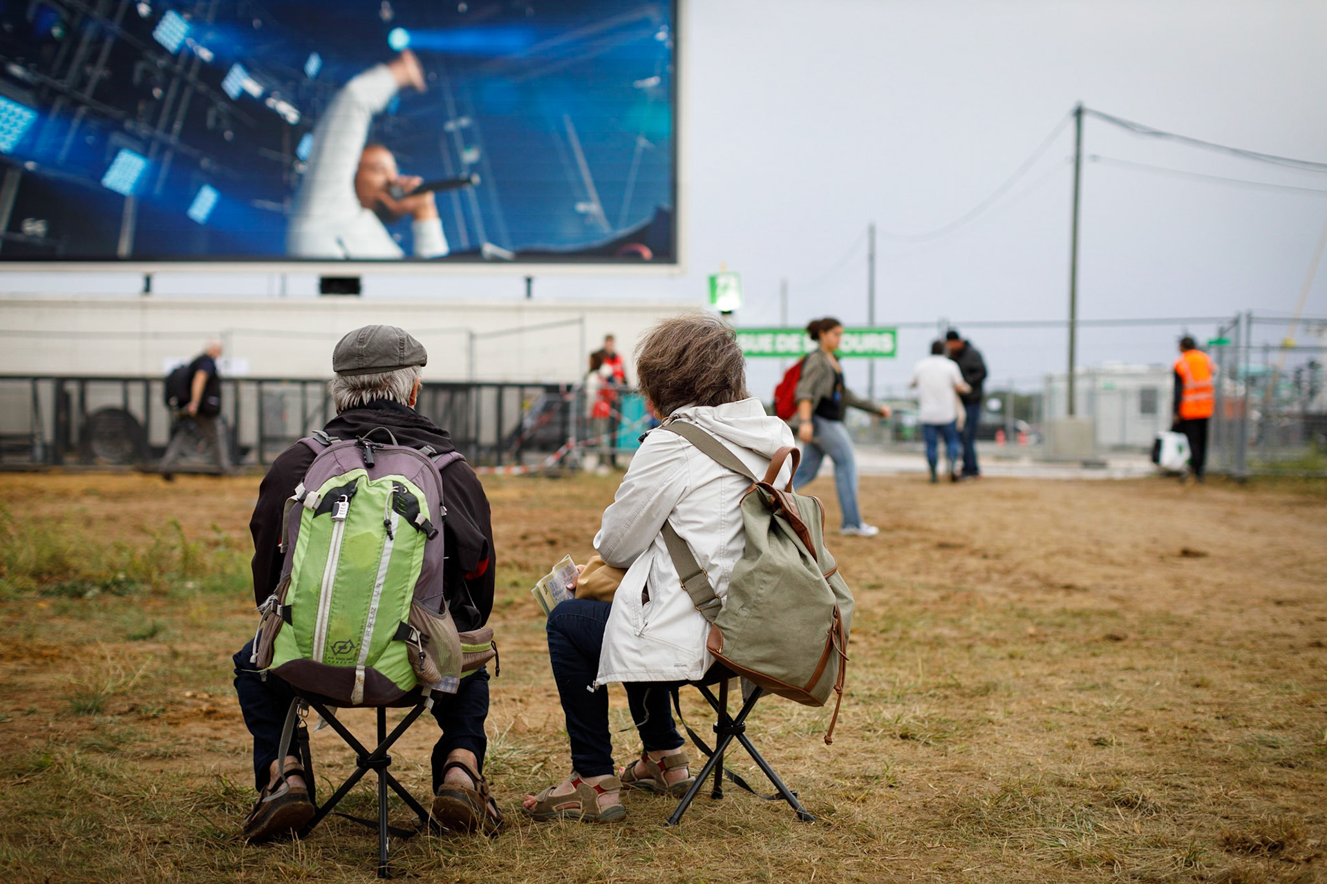Deux personnes écoutent, assis sur des tabourets pliants, un concert diffusé sur un écran lors de la fête de l'Humanité, le 9 septembre 2022, au Plessis-Pate. France, Le Plessis-Pate, 09-09-2022