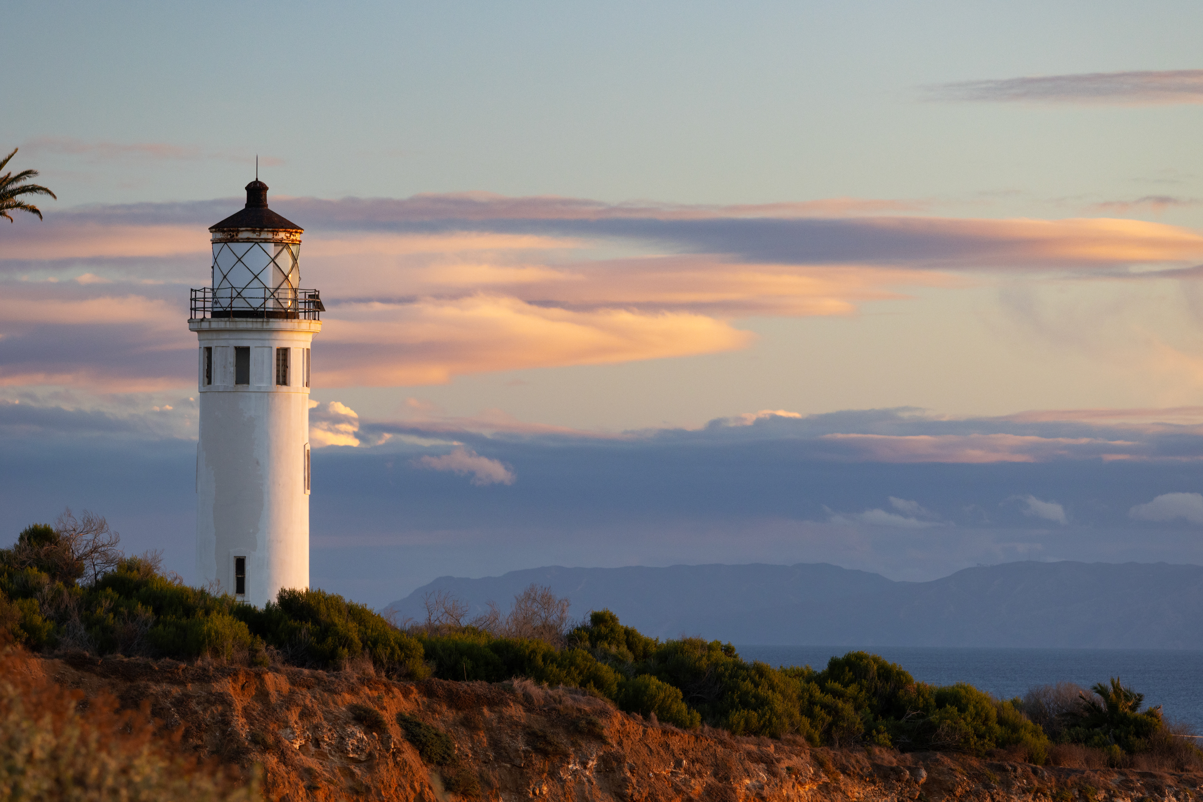 A lighthouse against a sunset sky with an island in the far distance.