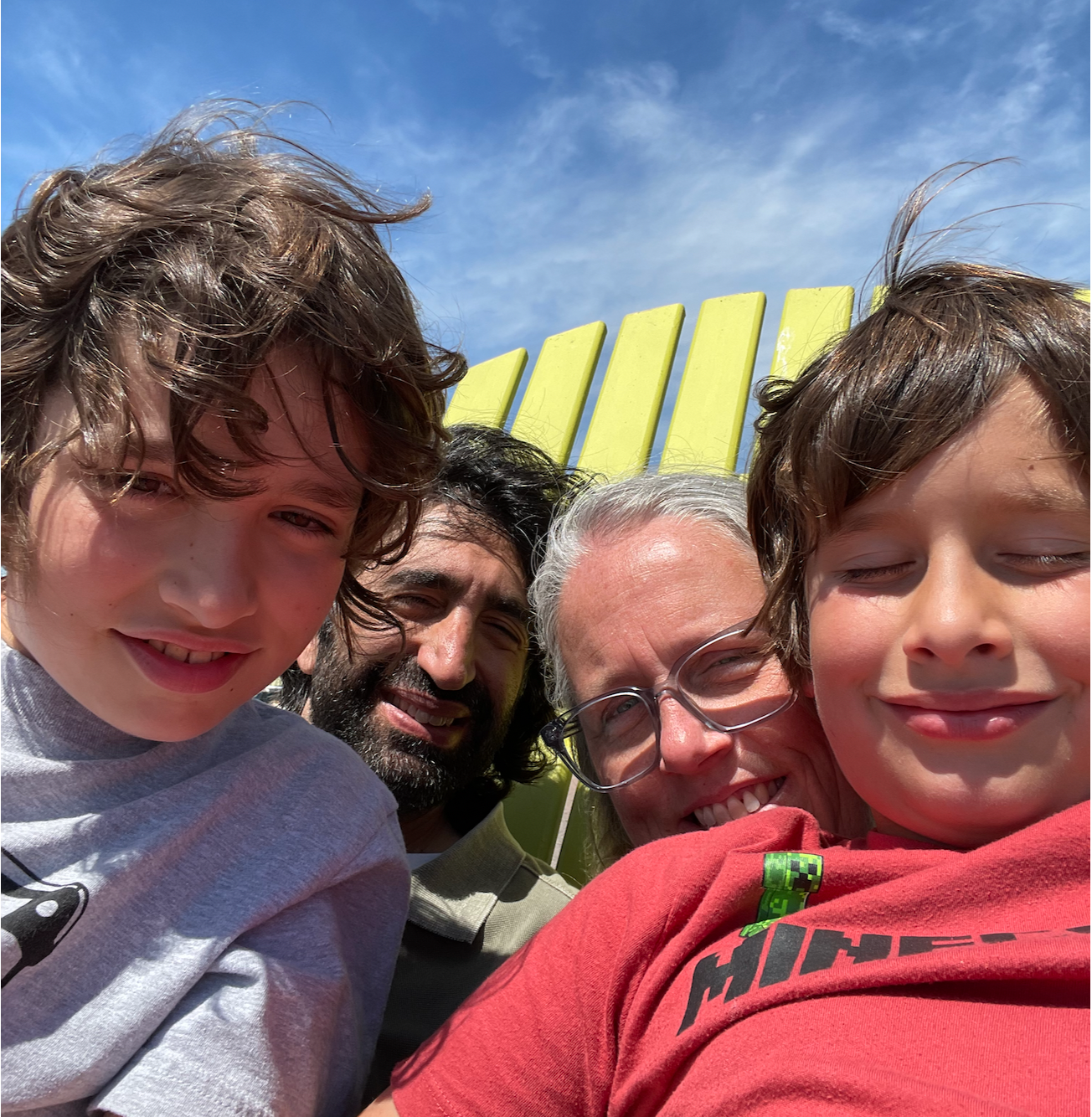 Family sitting on a large muskoka chair, outside blue sky. A mom, a dad, and two boys.