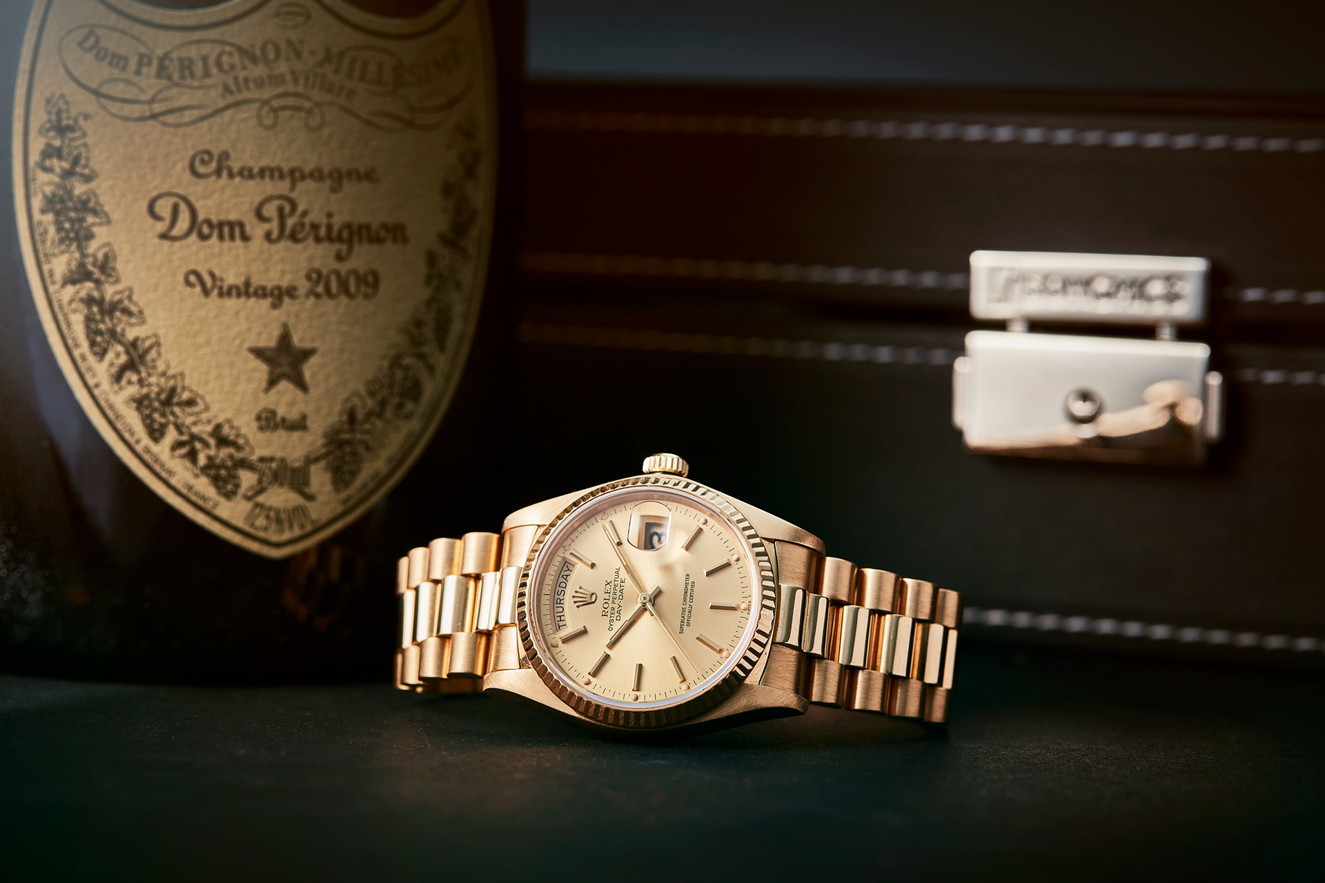 produktfoto einer goldenen rolex daydate vor einer flasche dom perignon