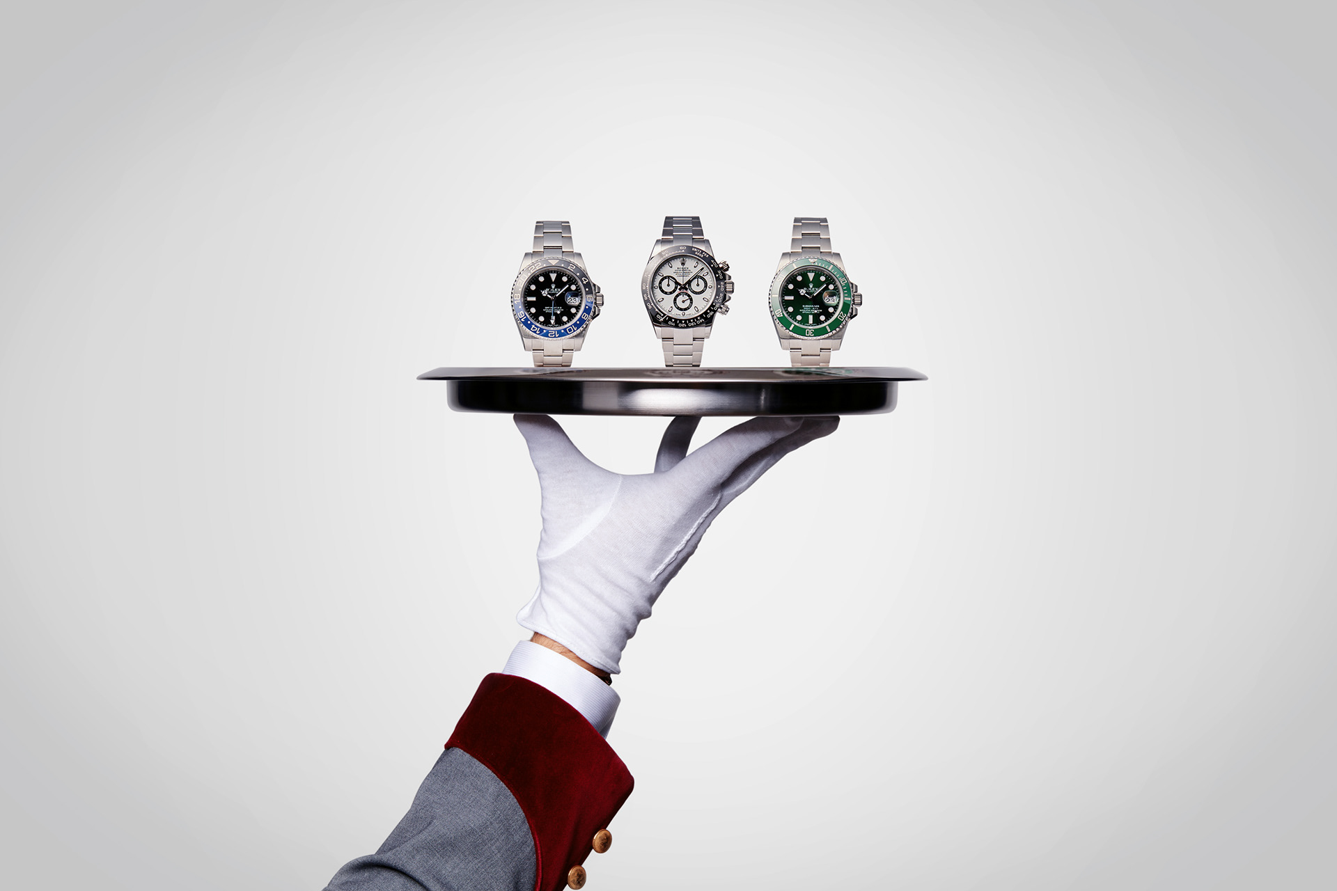 produktfotografie von drei rolex luxusuhren auf einem tablett getragen von einem pagen