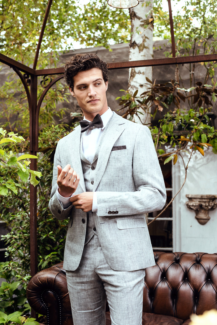 Mann im grauem Hochzeitanzug vor braunem Sofa draußen - Fashionfotografie