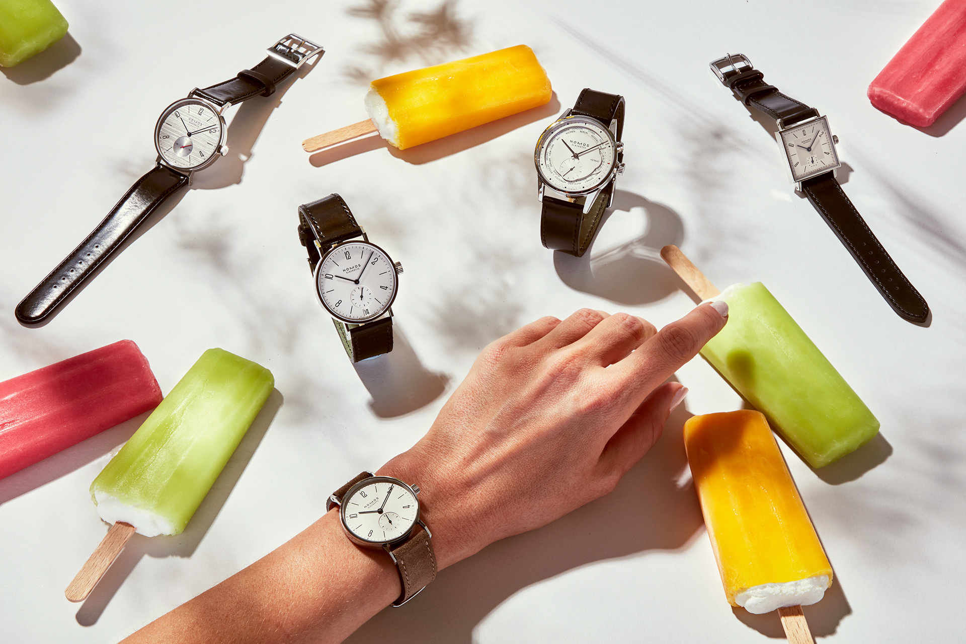 produktfotografie mehrer nomos luxusuhren mit eis am stil liegend auf einem tisch und frauenhand