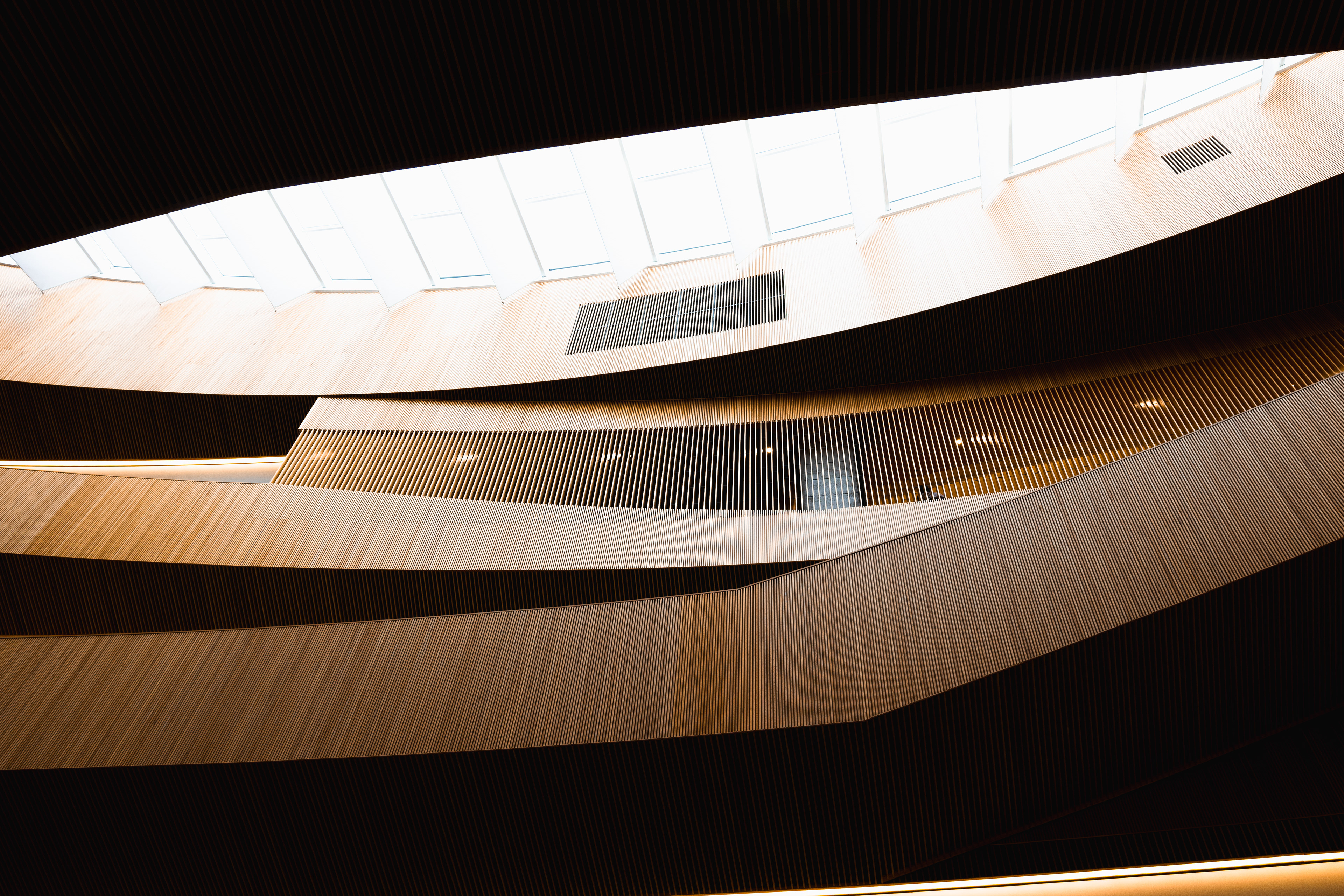 Looking up towards the huge glass ceiling and seeing the wooden layers intersect each other.
