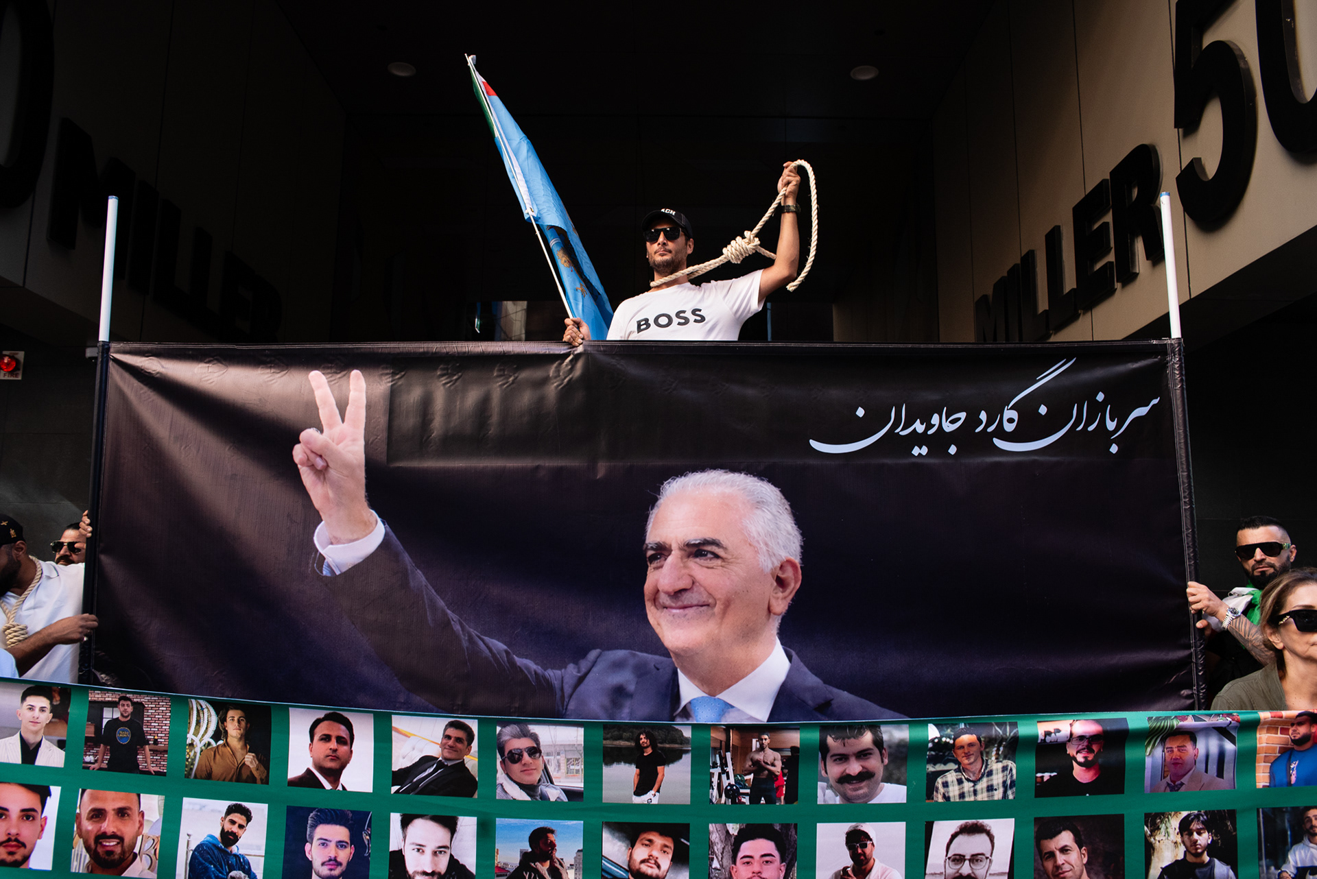 North Sydney, Australia. 11th Apr, 2026. A young man stands over a banner with the image of former Crown Prince Reza Pahlavi whiles pulls a rope tied around his neck at a rally outside the United States Consulate General at 50 Miller Street in North Sydney. The rally is part of a coordinated global day of action organised by parts of the Iranian diaspora supporting former Crown Prince Reza Pahlavi.