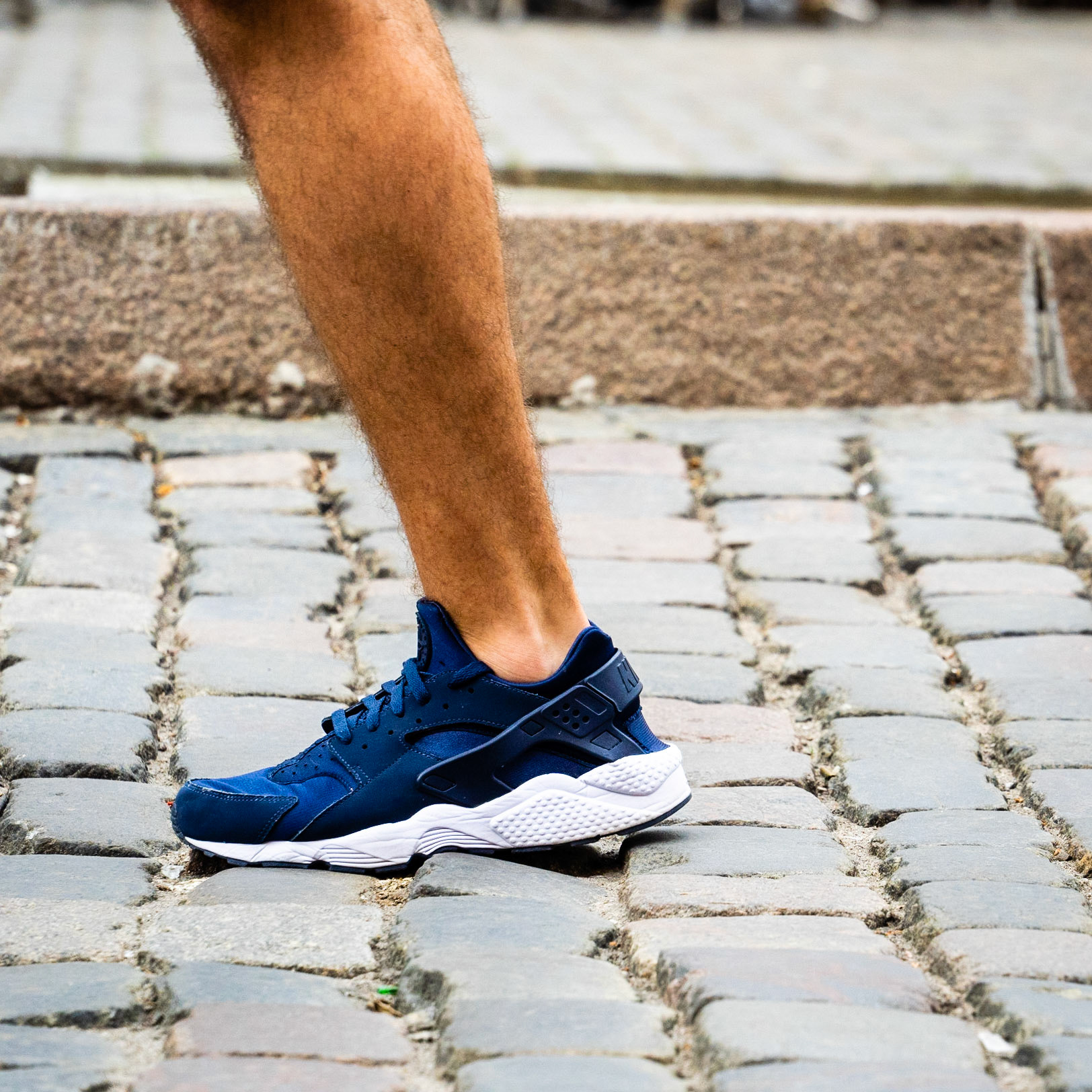 Tanned leg with blue sneaker on cobblestone pavement