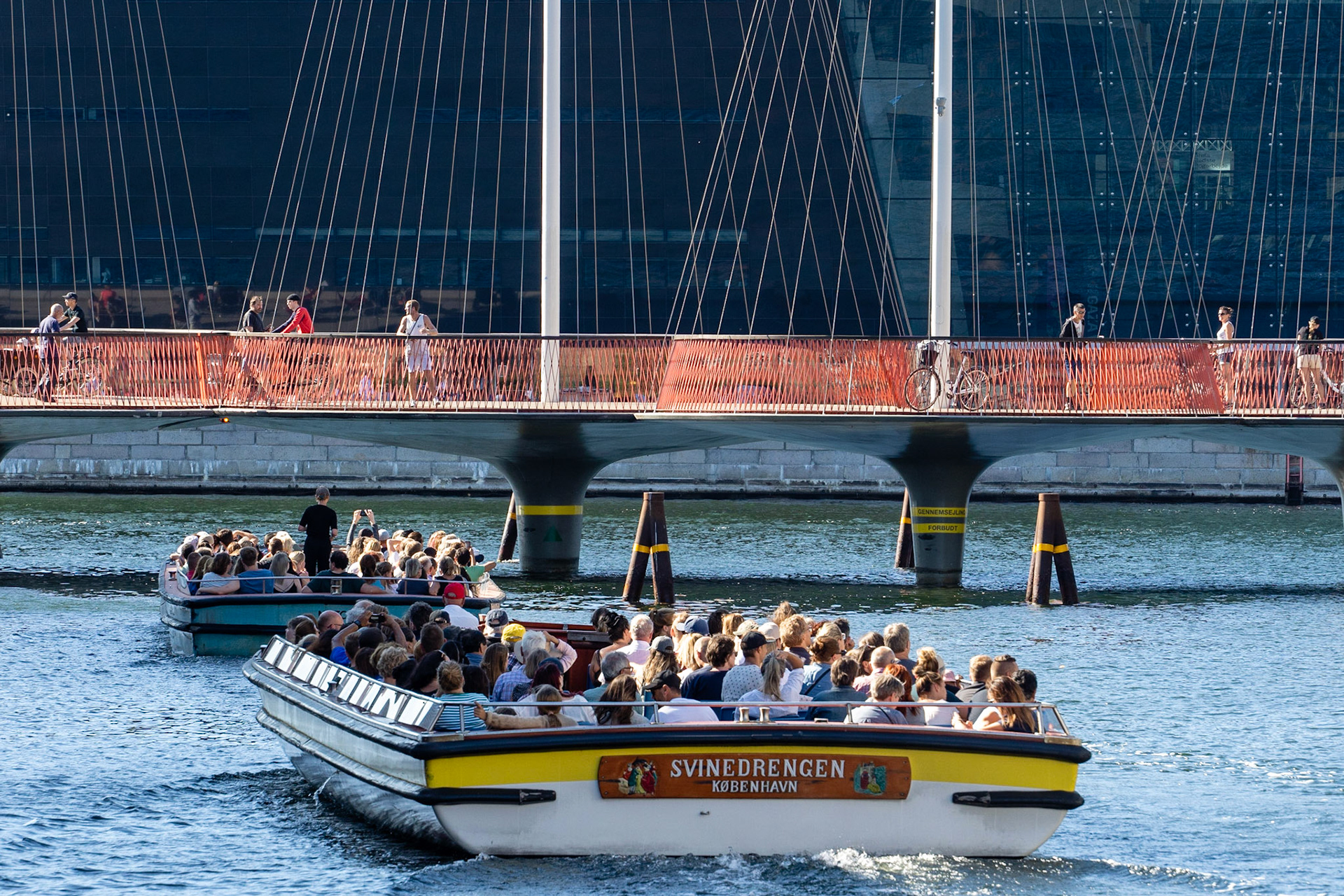 Canal tour boats approaching Cirkelbroen (Circle Bridge) in Copenhagn, architectural landmark by artist Olafur Eliasson, Royal Library in background