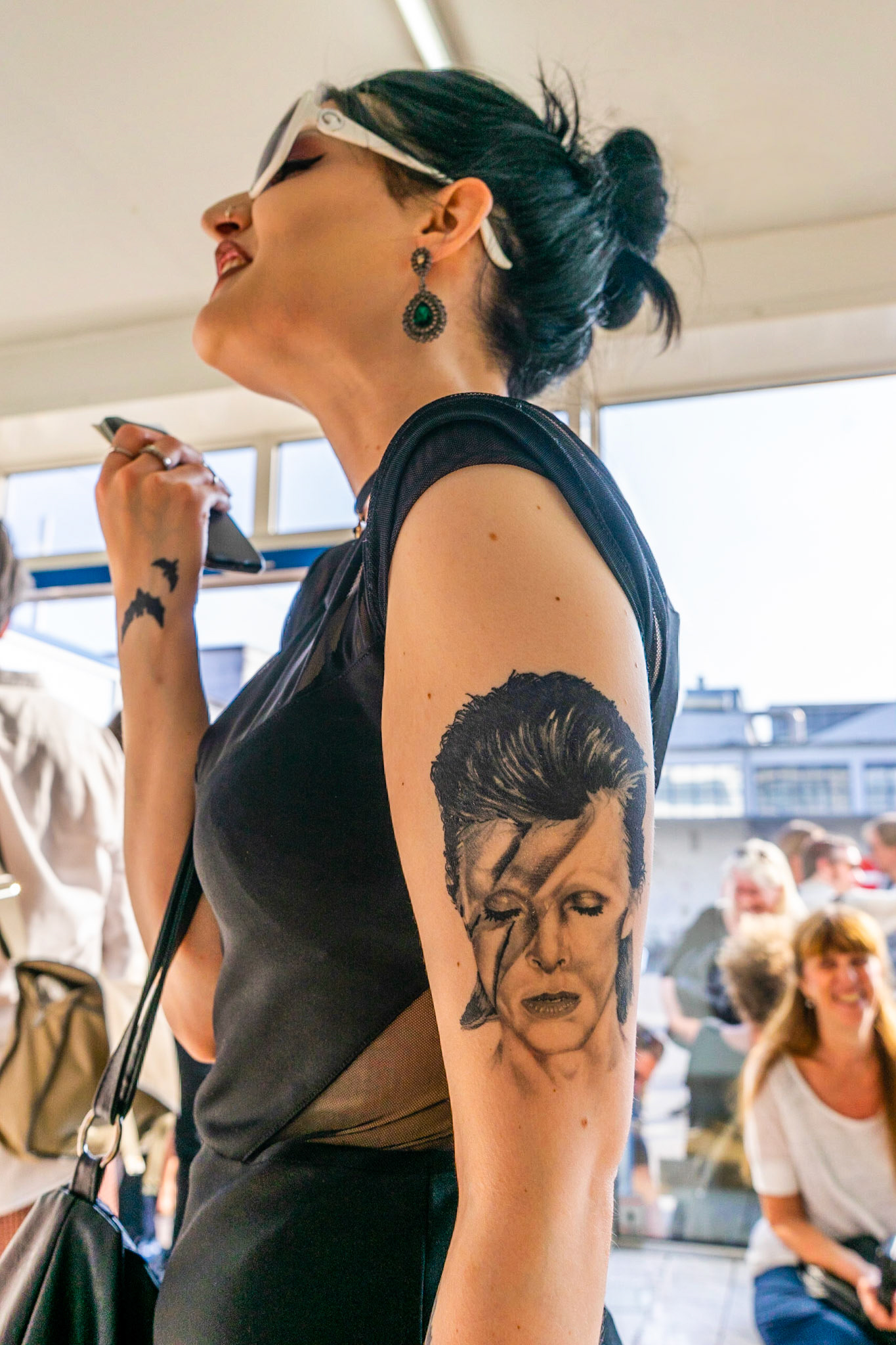 Young woman with tattoo of David Bowie on her upper arm wearing large white sunglasses