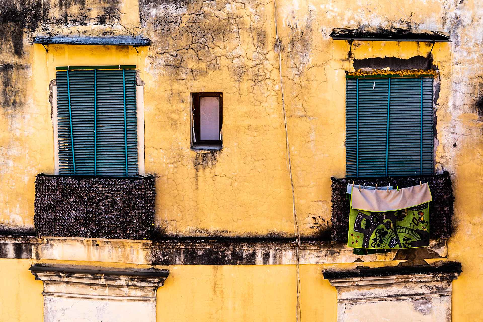 Balconies with turquoise blinds on wall with decaying yellow paint in Napoli historic centre