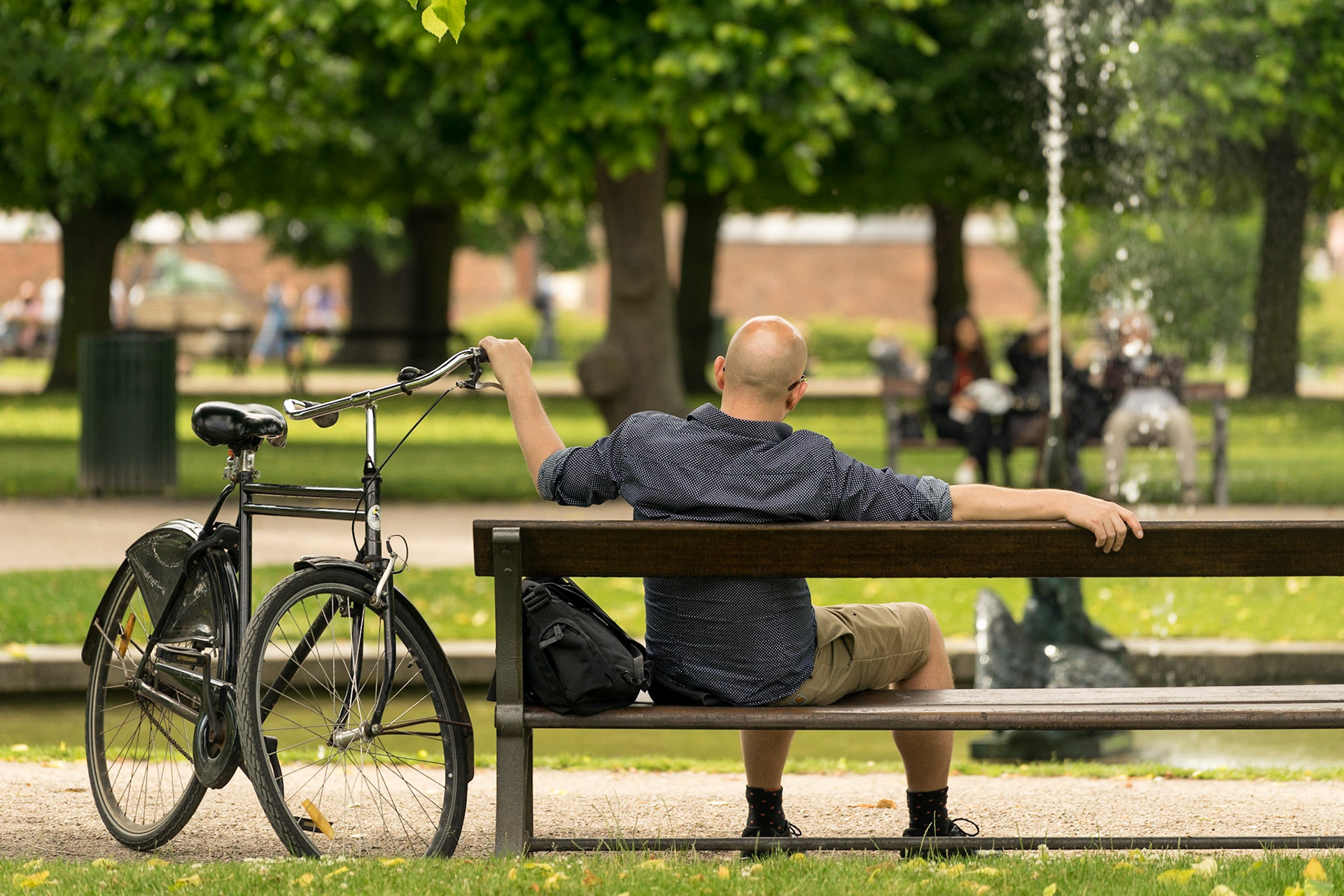 Man on bench relaxing, bicycle parked, in front of fountain in king's garden, copenhagen