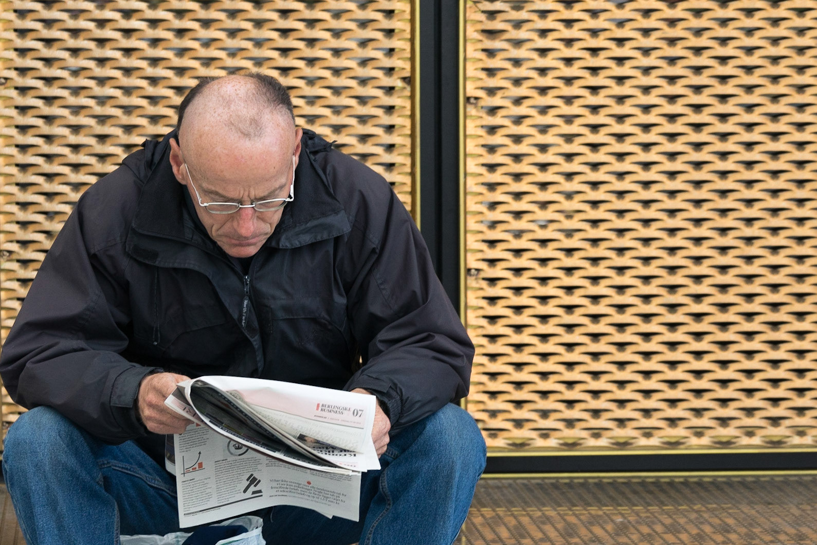 Man with glasses reading newspaper in front of grid wall