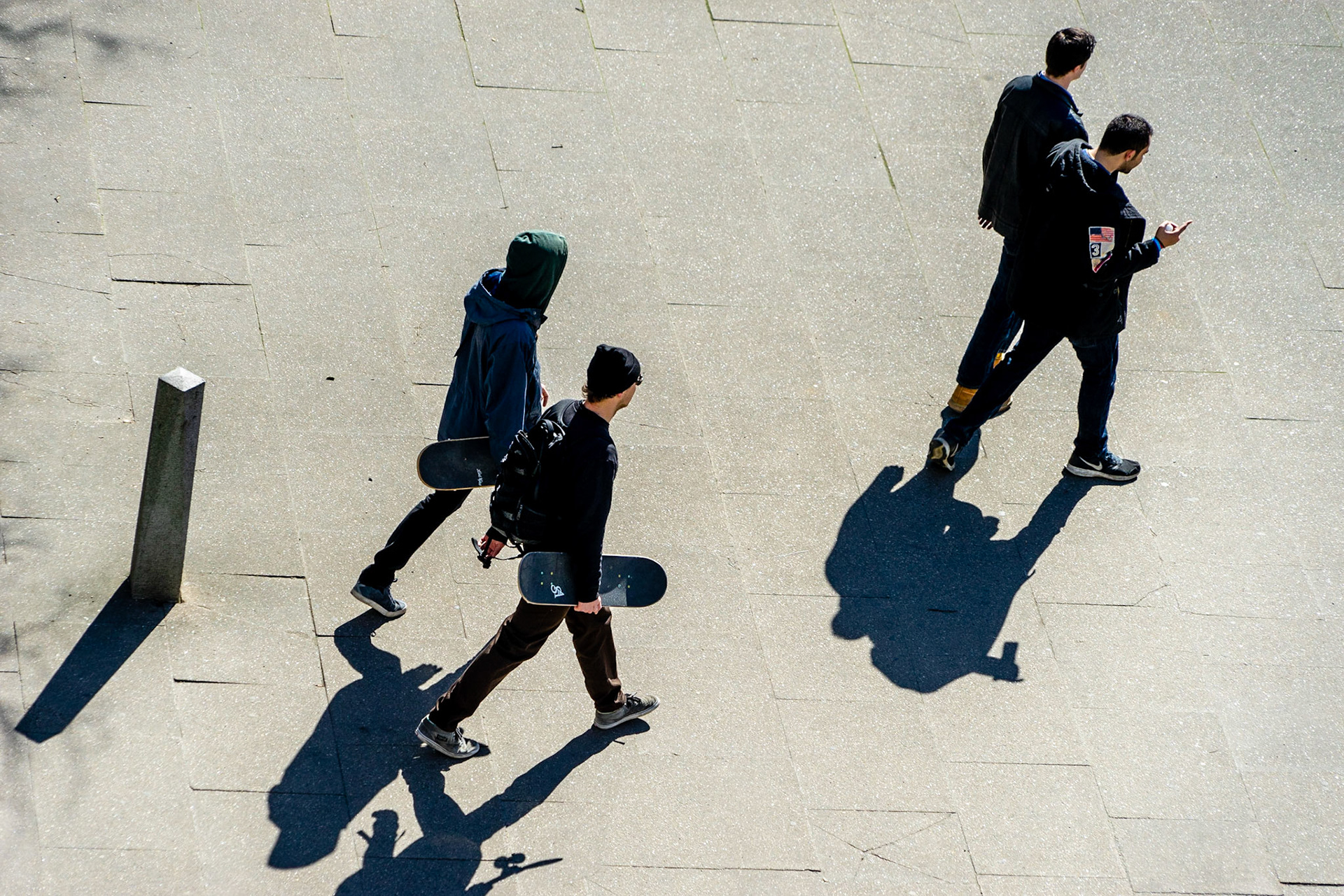 Square with trees casting shadows, seen from above, four men walking