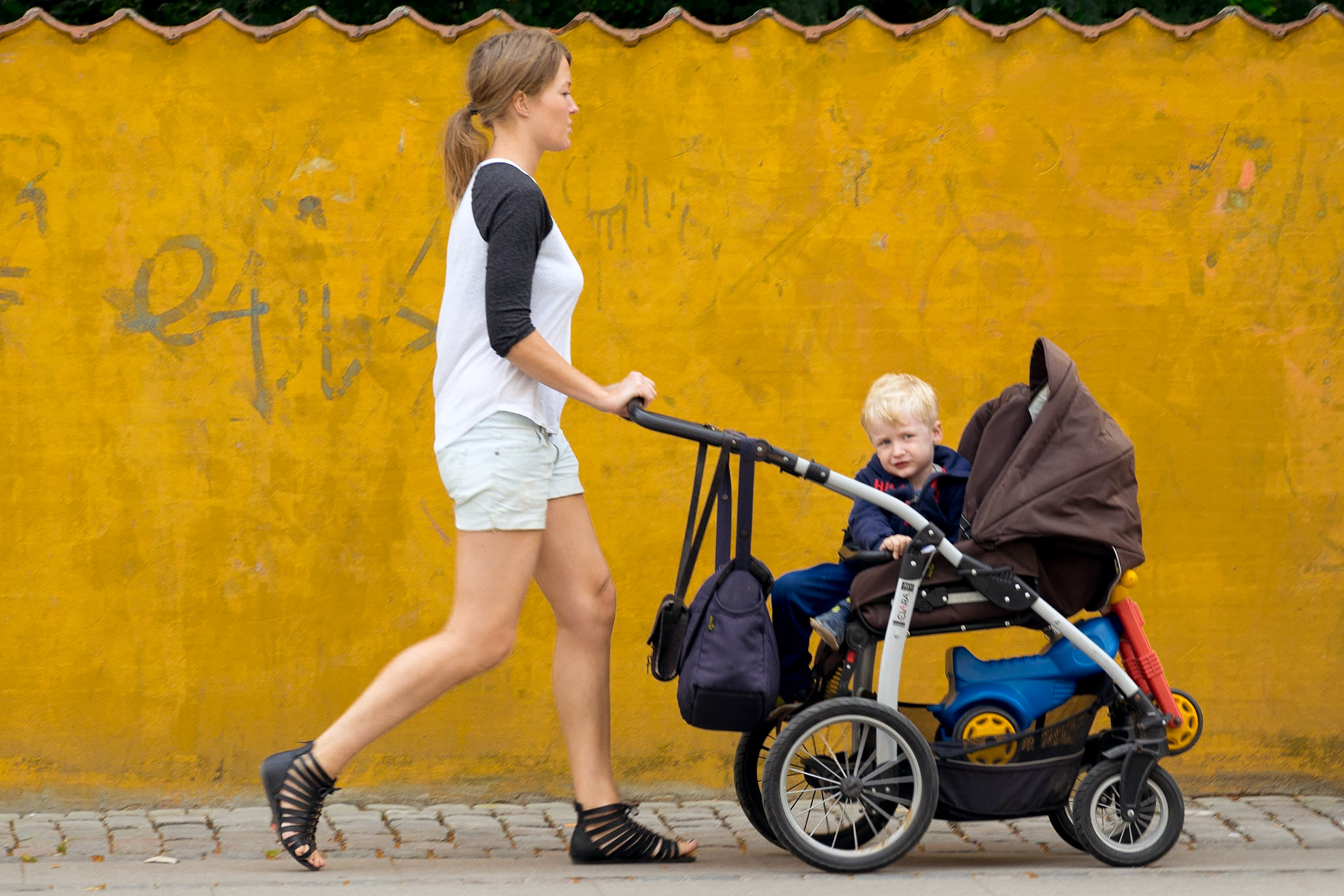 Woman with child in pushchair in front of yellow wall, Assistens Cemetray, Copenhagen