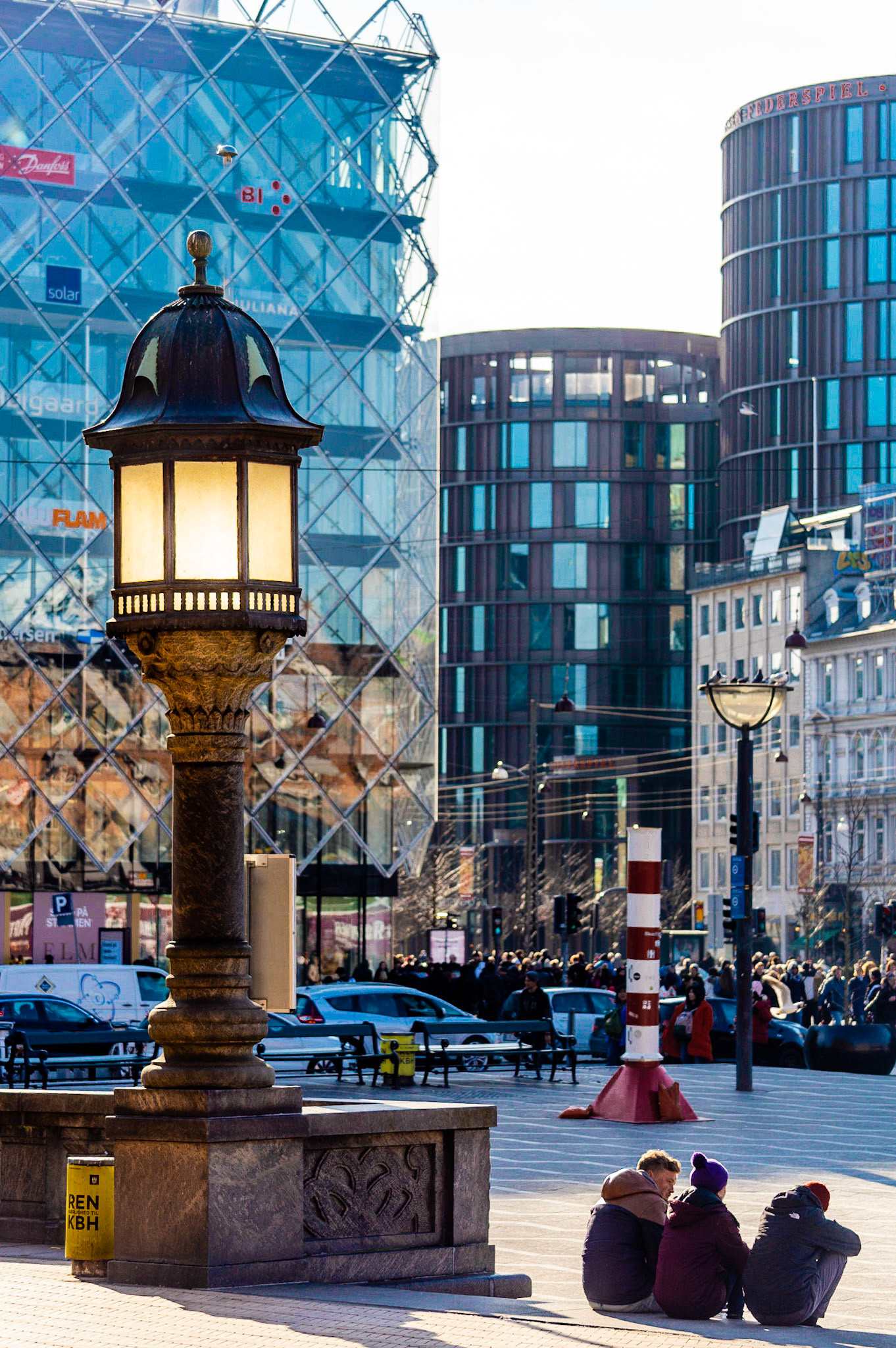 Copenhagen City Hall Square with retrofitted old gaslight, three people sitting, axel towers and Danish Industry in the background