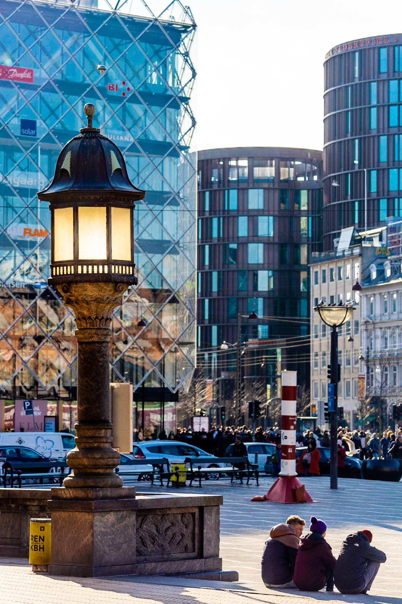 Copenhagen City Hall Square with retrofitted old gaslight, three people sitting, axel towers and Danish Industry in the background