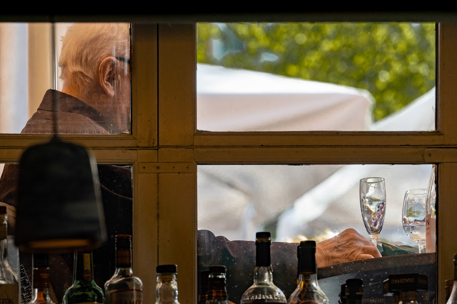 Man with glasses drinking, seen through window, bottles in foreground