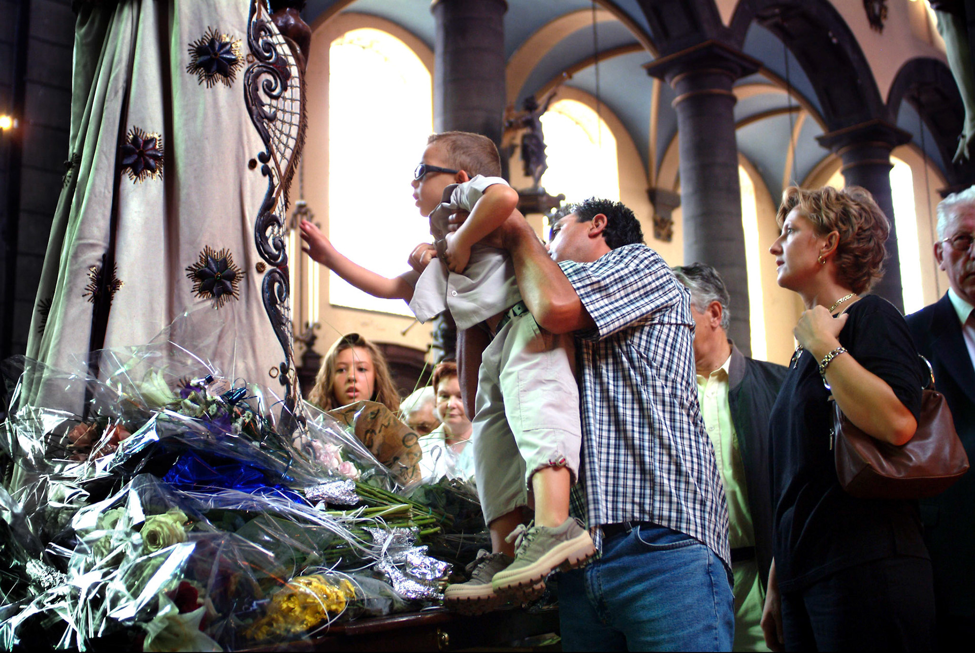 Jongen wordt door zijn vader omhoog getild om bij Maria te komen. Het is bruikelijk tijdens deze verering om het beeld van Maria even aan te raken. Saint Marie feesten, Maria verering na de Processie in Luik (Autres Meuse) 15-8-2003