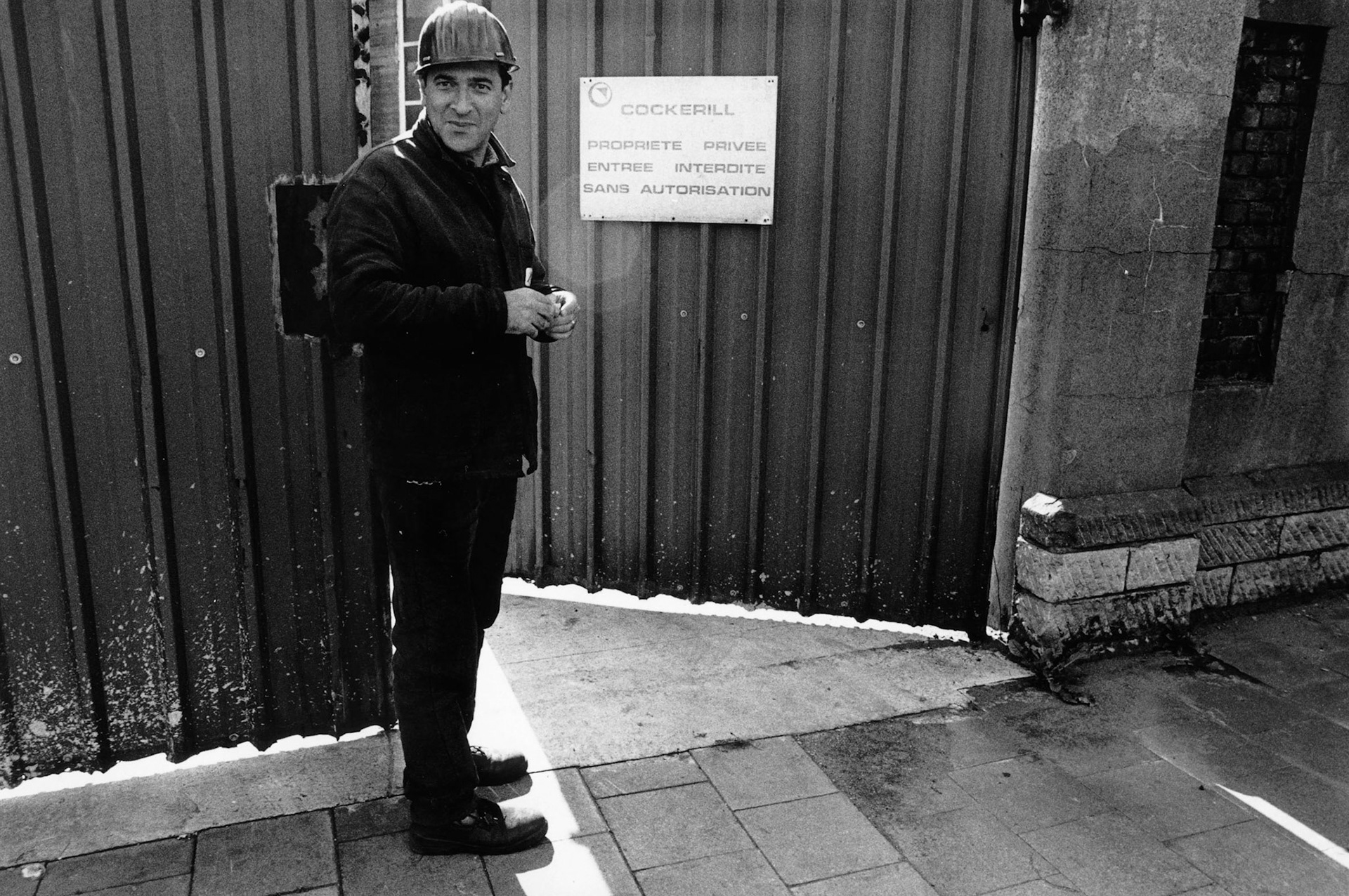 Fabrieksarbeider neemt pauze buiten fabriekspoort. Seraing, nov. 2002. "Onder industrieele vleugels" Maassteden in Wallonie.