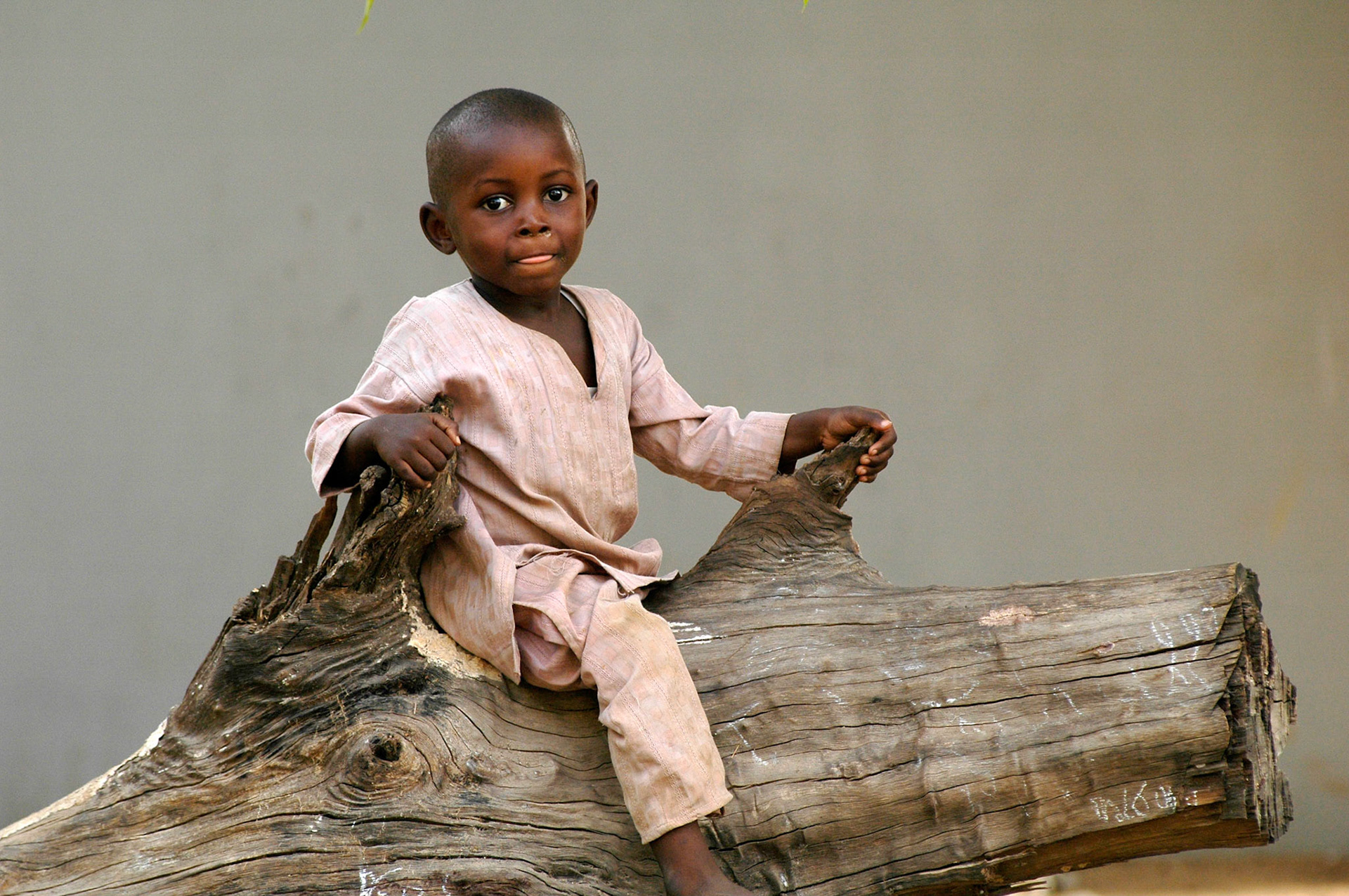 Kind speelt in de tuin op een boomstronk, Kaduna (Nigeria) 8 april 2006