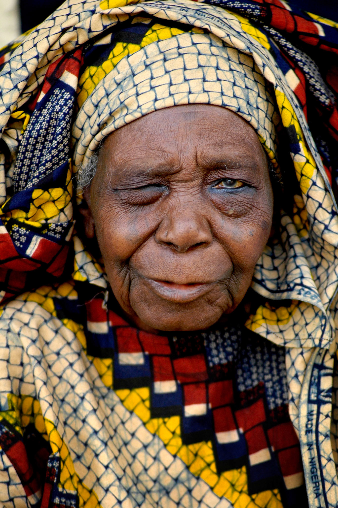 Oude vrouw met oogklachten in traditionele kleding wacht bij Almadina Pharmacie op behandeling, Zaria (Nigeria) 11 april 2006