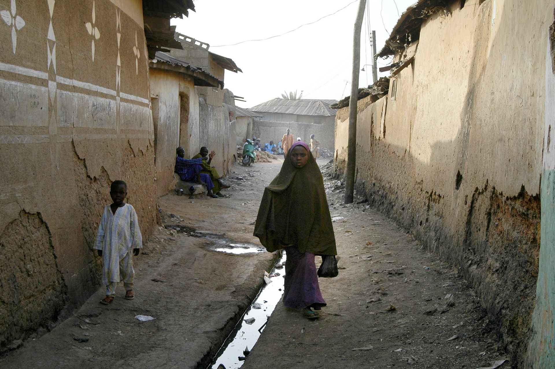 Jonge vrouw loopt in de oude stad van Zaria langs het open riool. Zaria (Nigeria) 11 april 2006