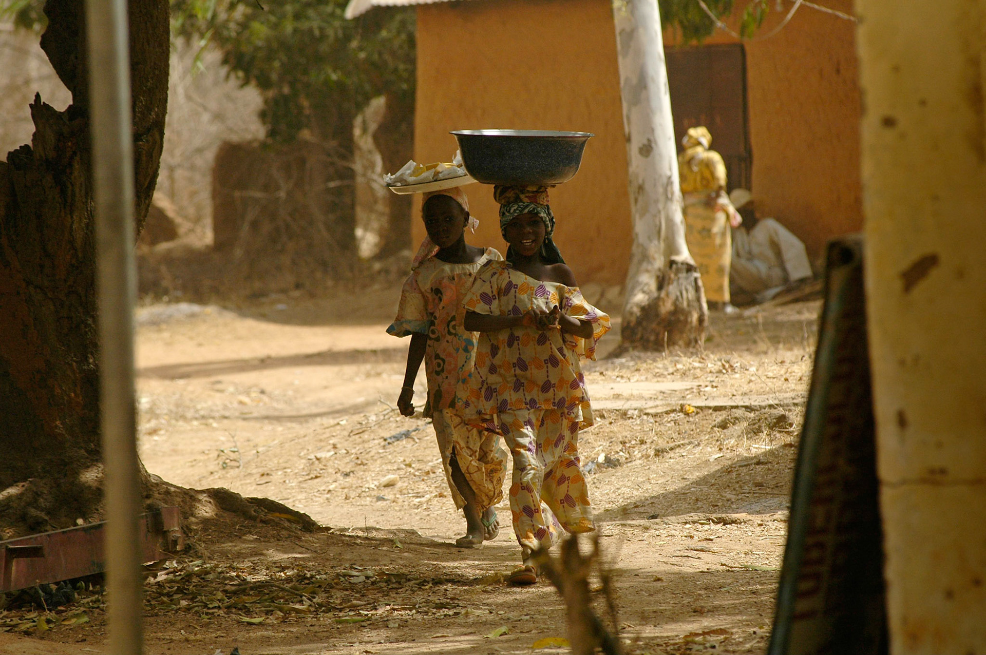 Jonge meisjes met pannen op hoofd lopen door het woongebied bij het NTBLTC Lepra en TBC hospital, Zaria (Nigeria) 11 april 2006