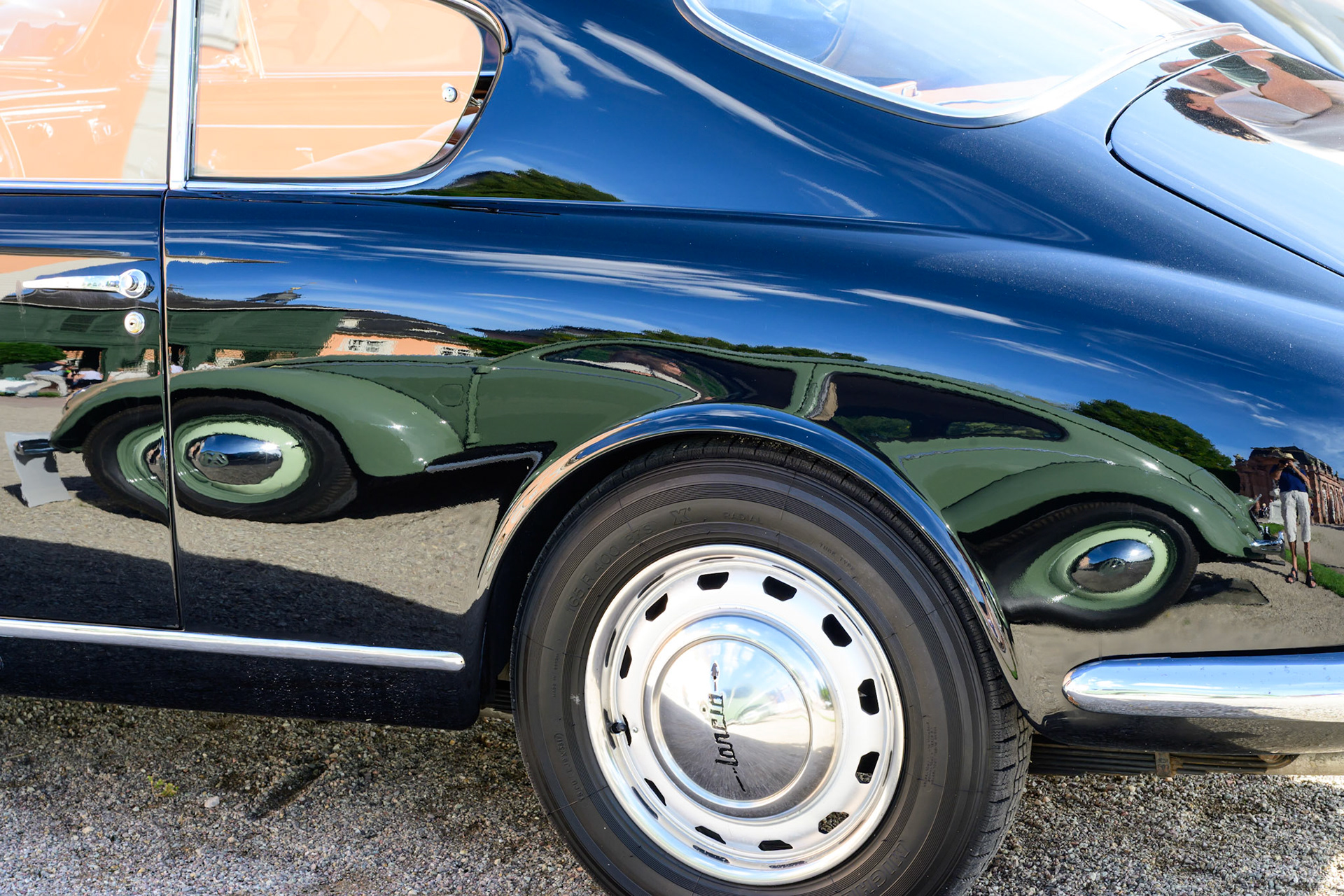 Ein grüner VW Käfer spiegelt sich in der schwarzen Karosserie eines Lancia