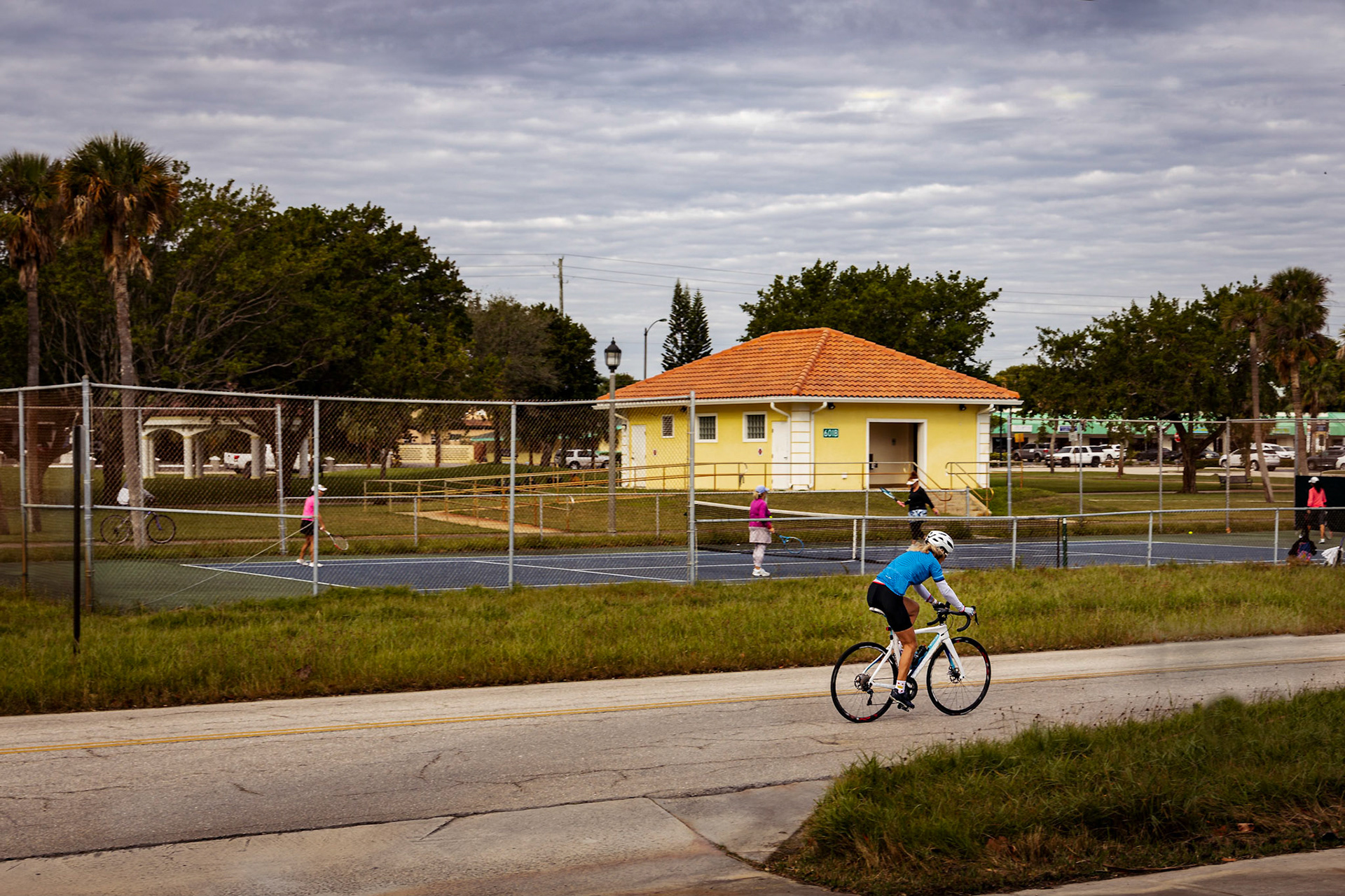 Cyclist passing people playing tennis.