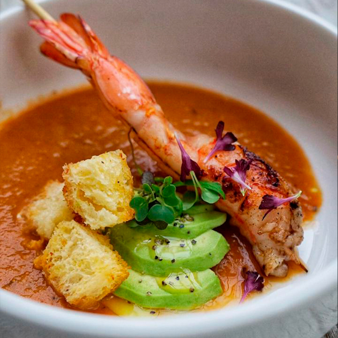 Bisque, sopa con fondo de mariscos, tomates san marzano rostizados, jerez y toque de leche de coco con langostino marinado en cítricos y asado