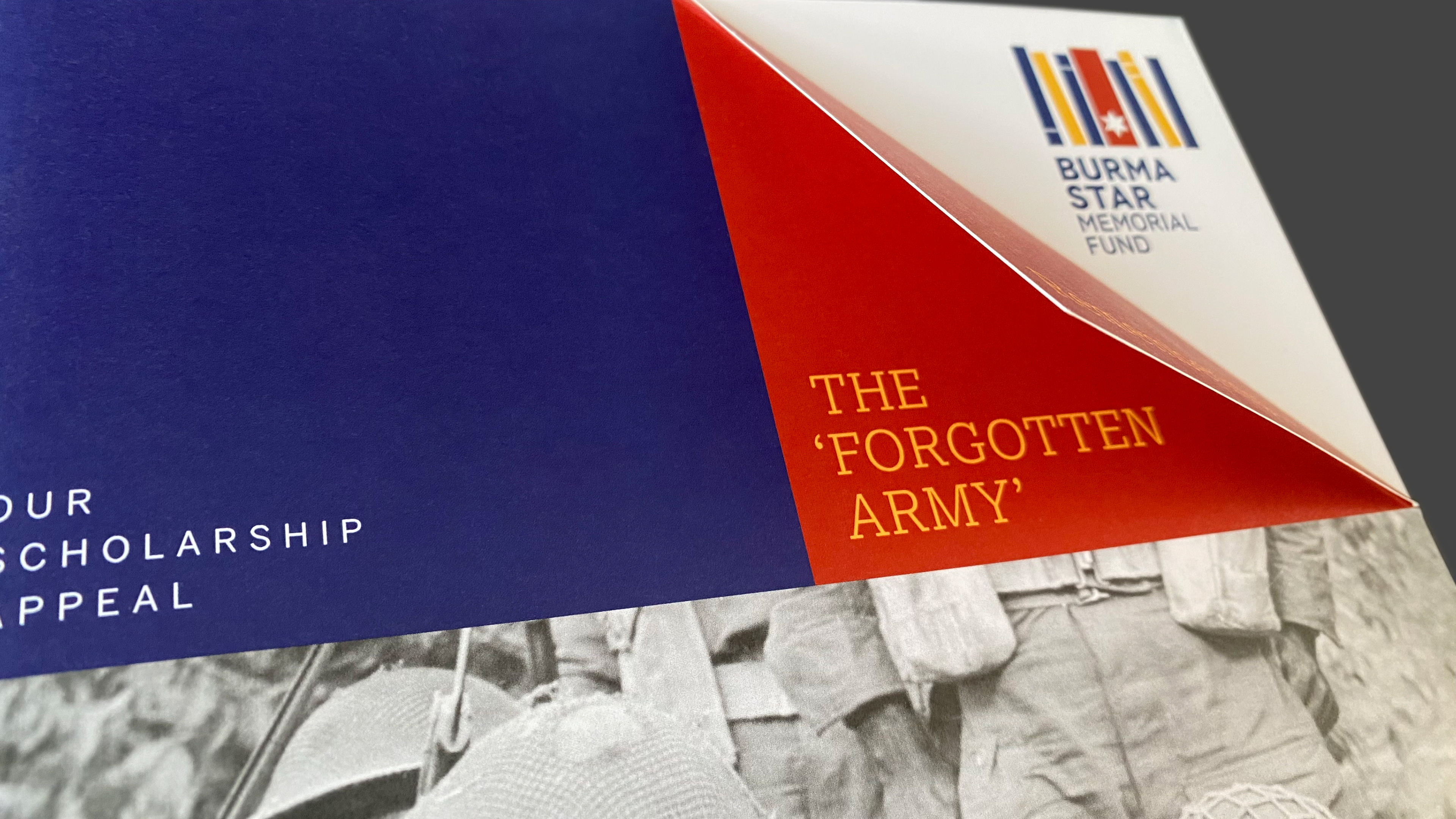 Front cover of the Burma Star Memorial Fund Scholarship Appeal brochure titled 'Remembering the Forgotten Army'. The corner of the brochure cover  is folded over as an aide memoire. 'Remembering...' is visible to the viewer while the rest of the title is revealed underneath the fold. 