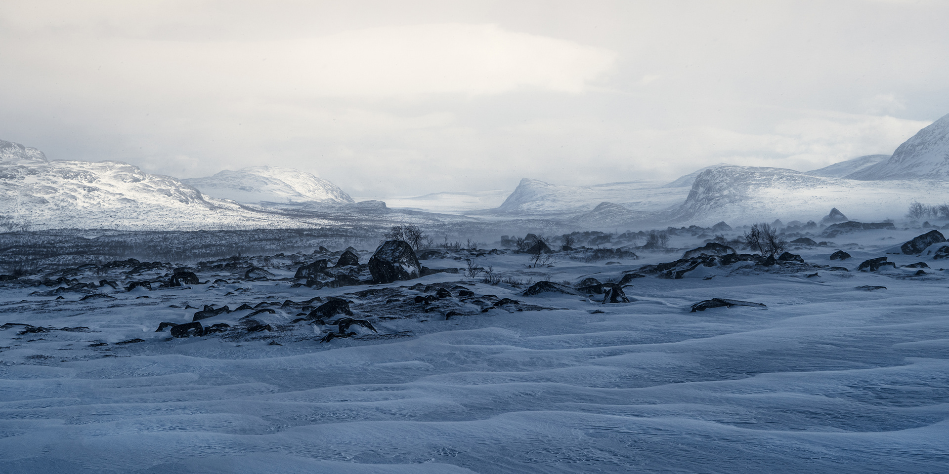 Monochromatic landscapes of the Swedish Artic on a hazy day. Windswept snow patterns in the foreground and fells in the distance.
