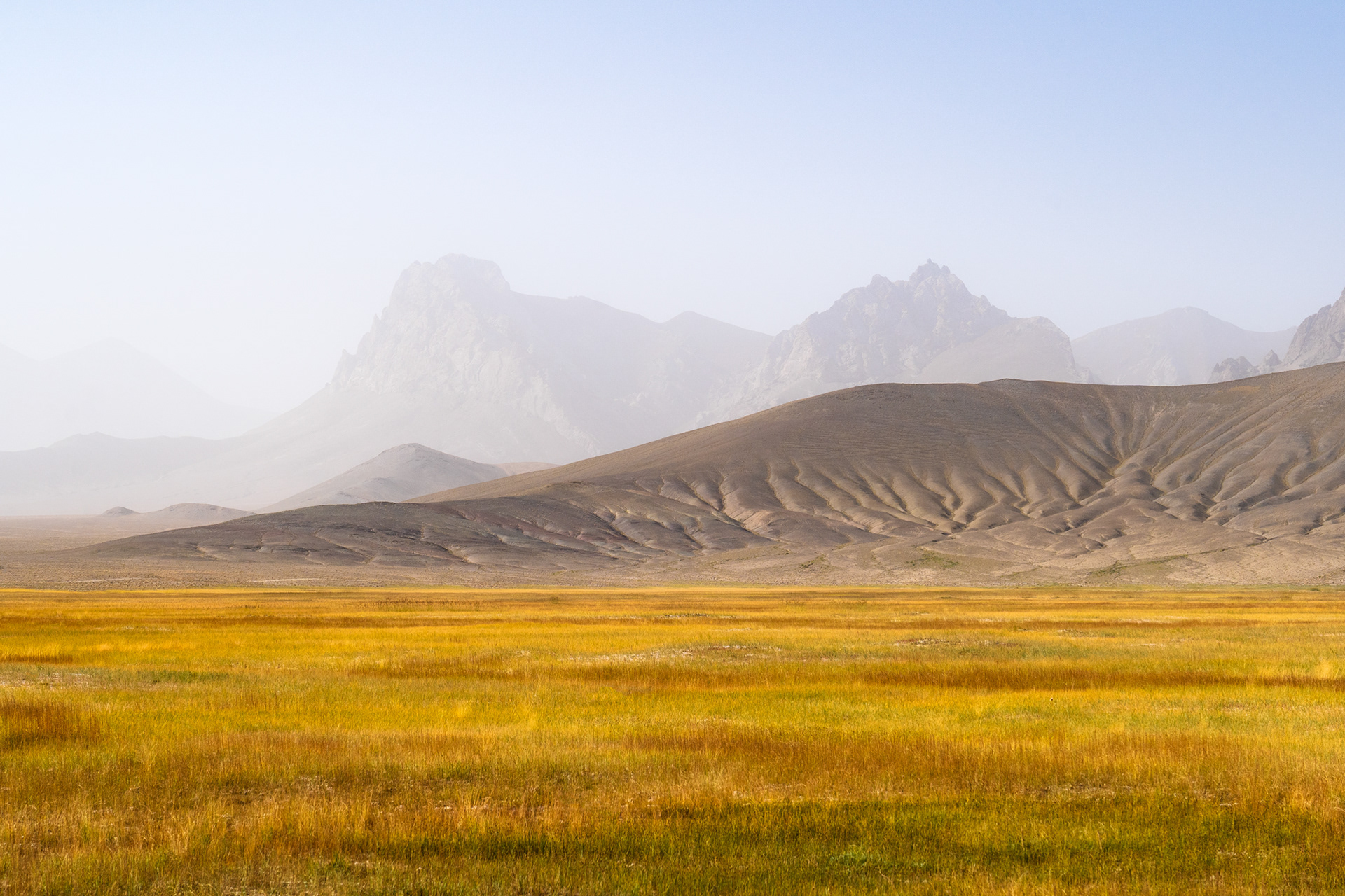 Rugged peaks rise from the haze above the colourful grasses of Rangkul, Pamir, Tajikistan