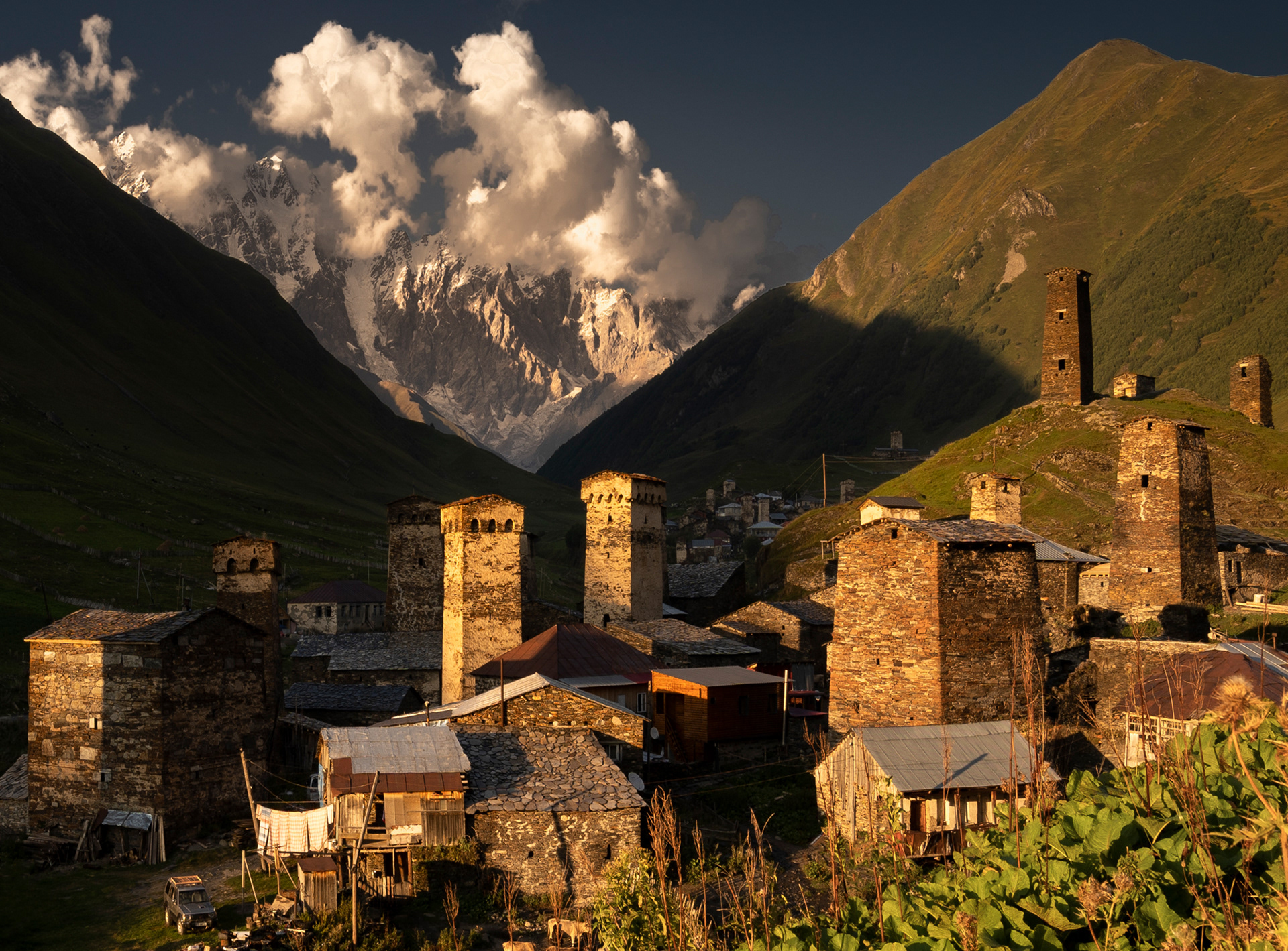 A sunset over a mountainous village, with ancient defensive stone towers.