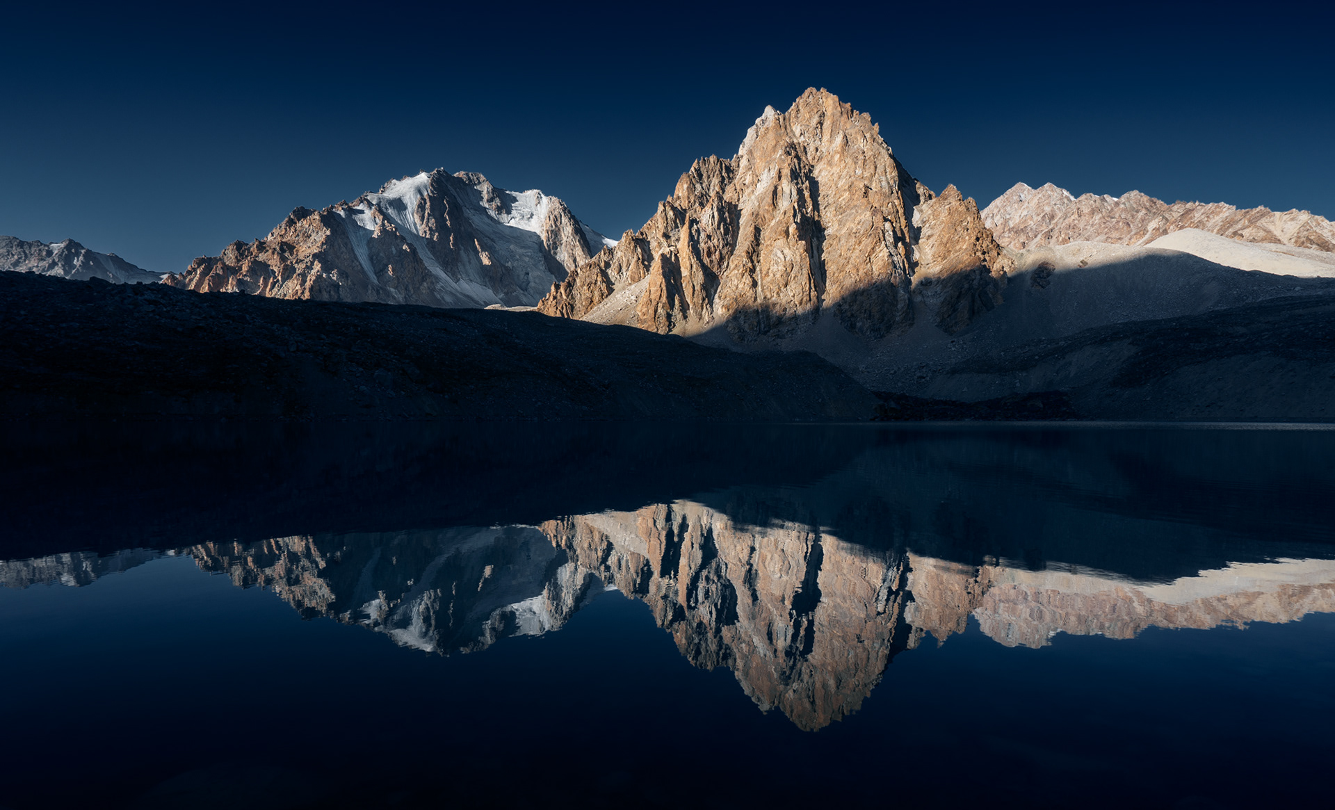 A sunrise mountain is reflected in a mirror-like Tsaxinkul lake.