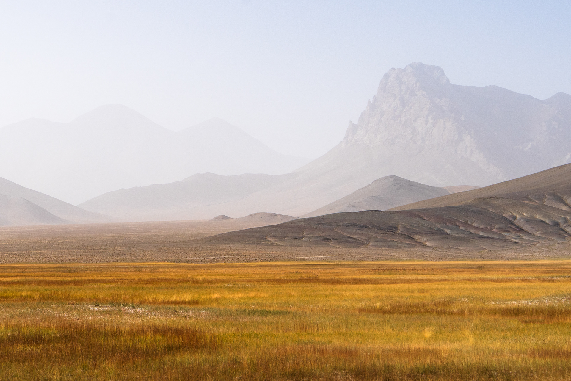 A hazy day in a rugged mountainous terrain, with colourful grasslands.