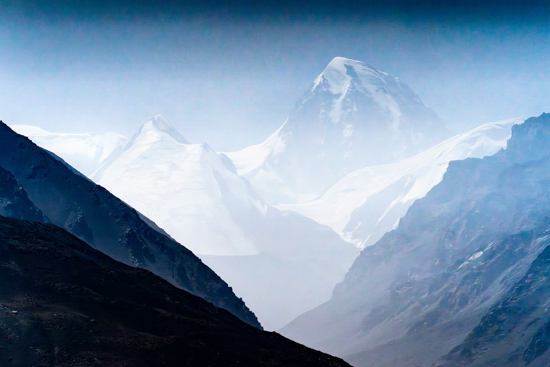 A hazy photography of Shah Dhar, a 7,038m tall peak in the Pakistan Hindu Kush, seen with Afghan peaks in the foreground.