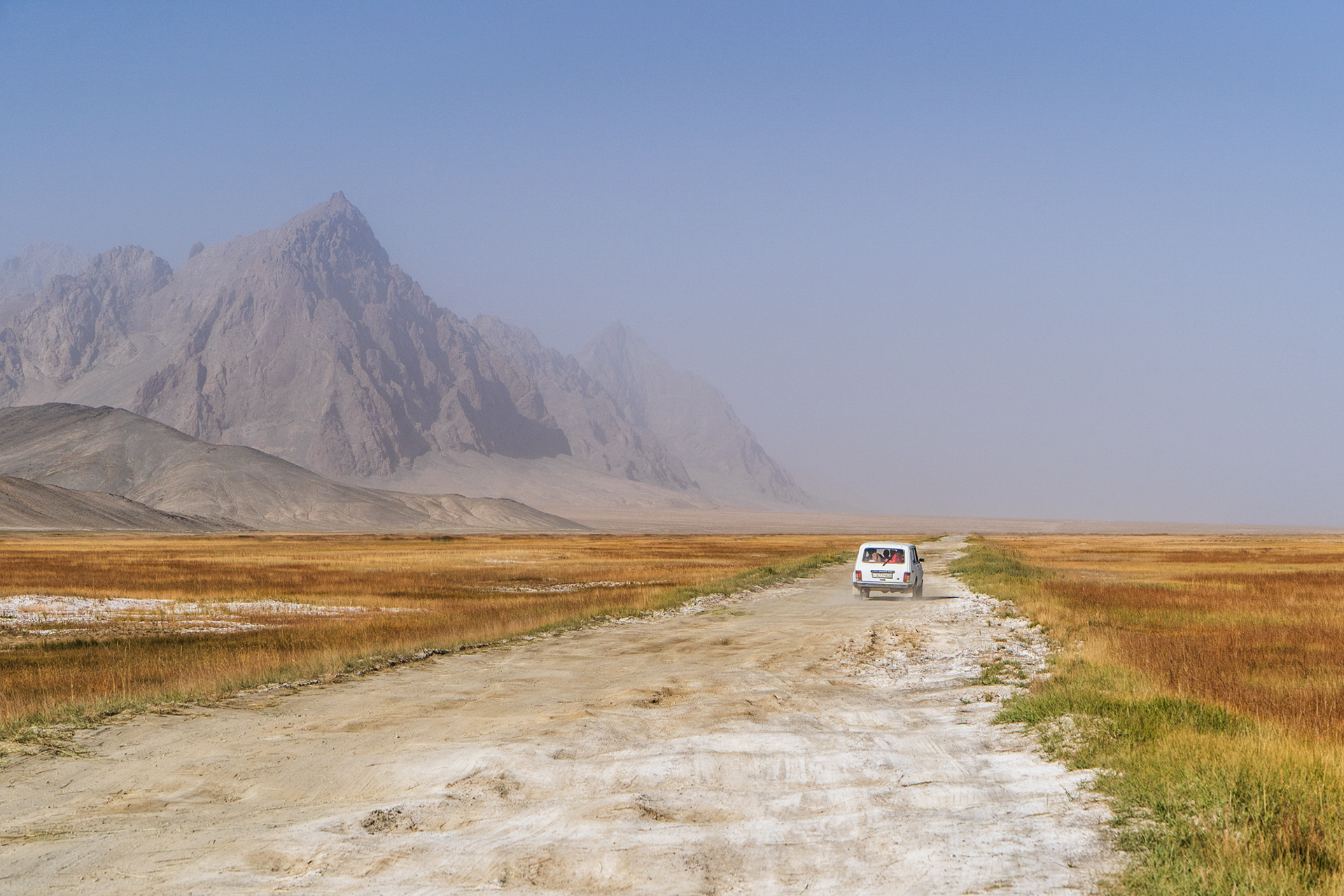 A soviet-era Lada drives along the bumpy road through the hazy, rugged landscape between Rangkul and Murghob, Eastern Pamir, Tajikistan