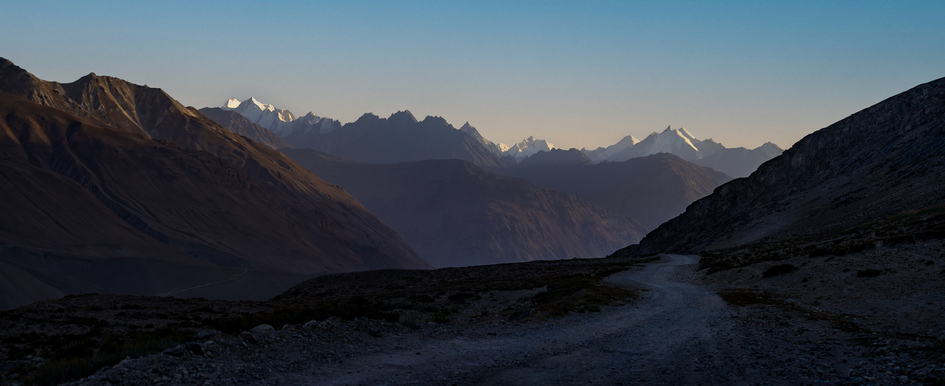 A panoramic photo of 6,000+ meter mountains in Afghanistan as seen from Tajikistan during an evening sunset.