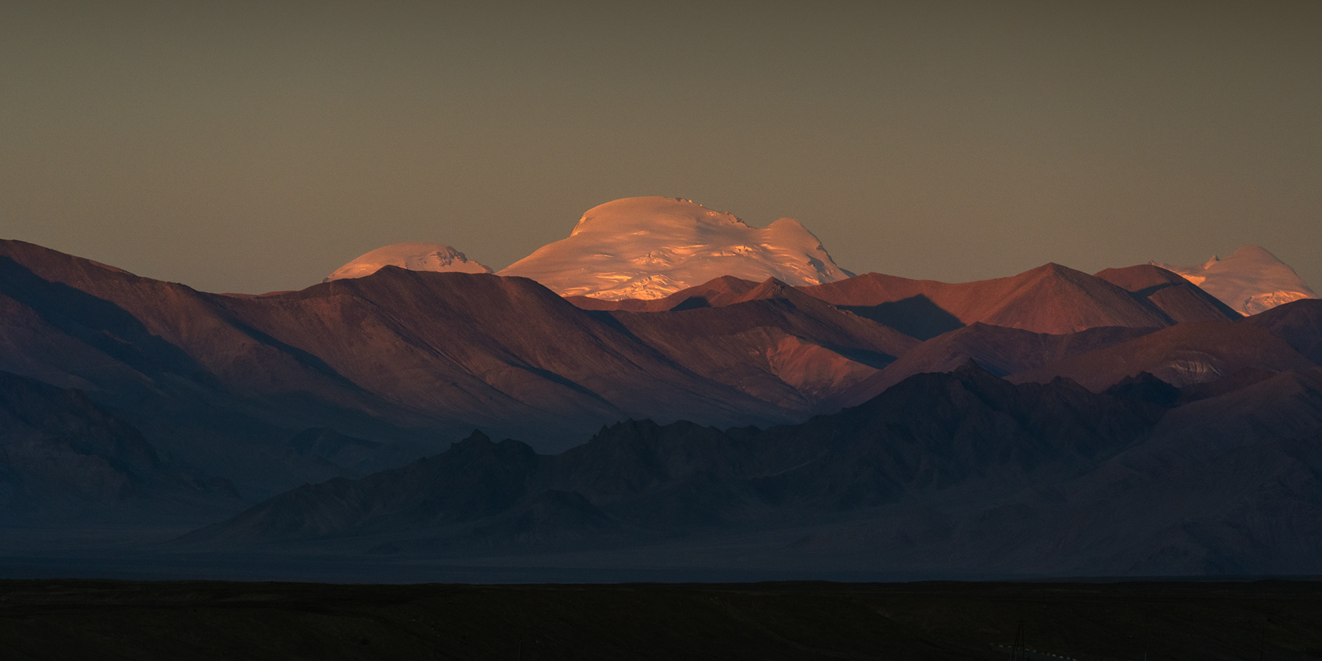 A snowy glaciated mountain called Muztagh Ata catches the last rays of sun.