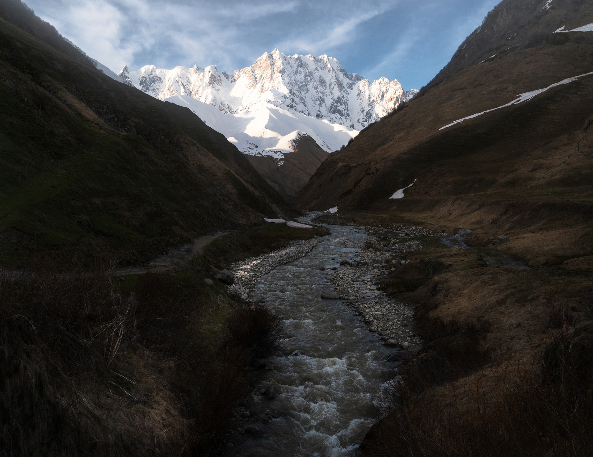 A river in a mountainous area with a tall, snowy mountain in the background.