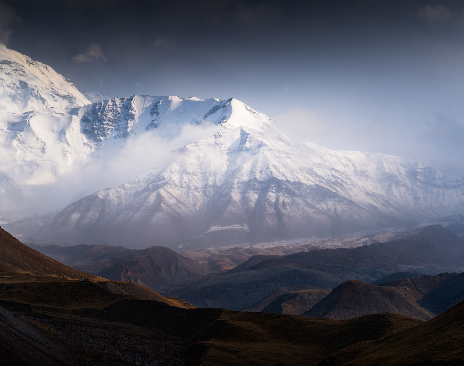 The misty lower faces of Peak Lenin are hit by the rays of the sunset after a storm, Pamir Mountains, Alay, Kyrgyzstan
