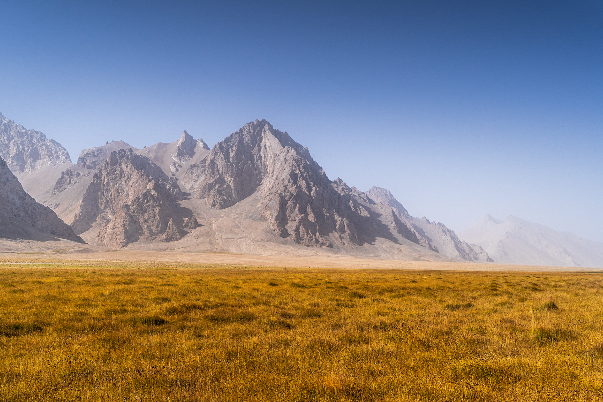 A hazy day in a rugged mountainous terrain, with colourful grasslands.