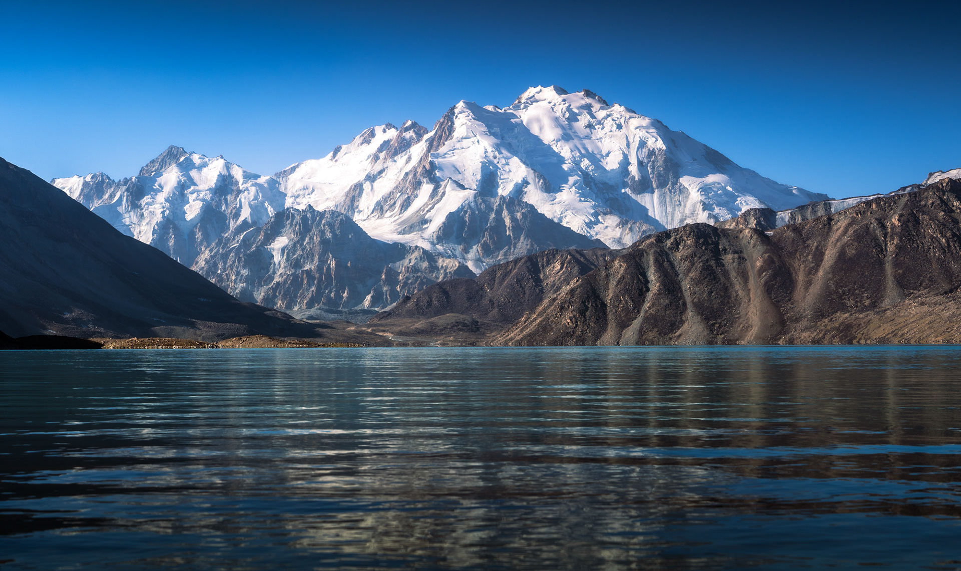 Sunrise hits the glaciated mountain above a lake.