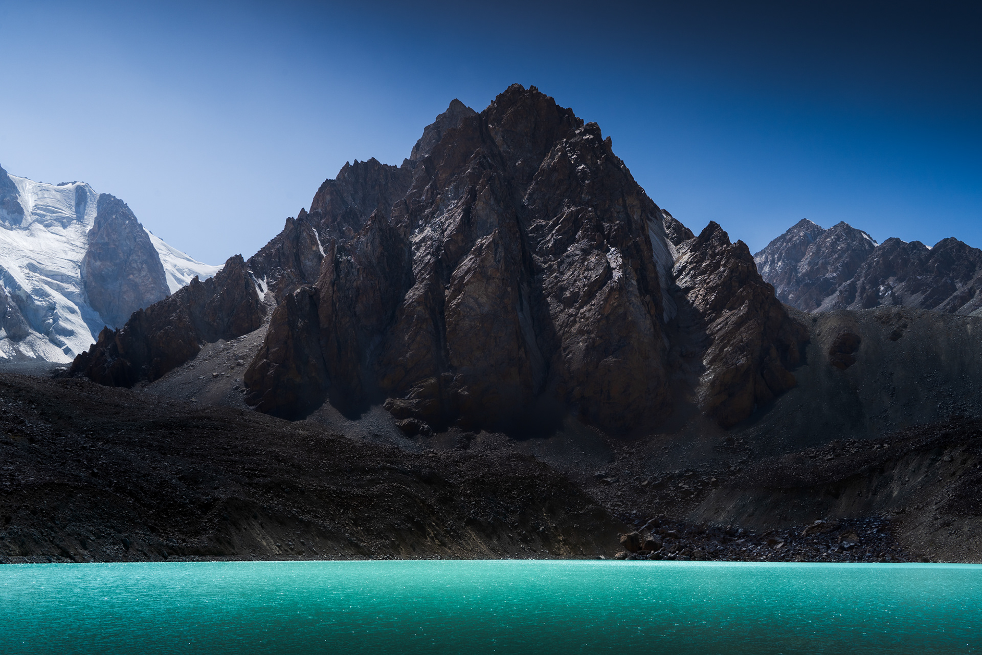A dramatic peak rises above a sun-illuminated lake called Tsaxinkul in Tajikistan.