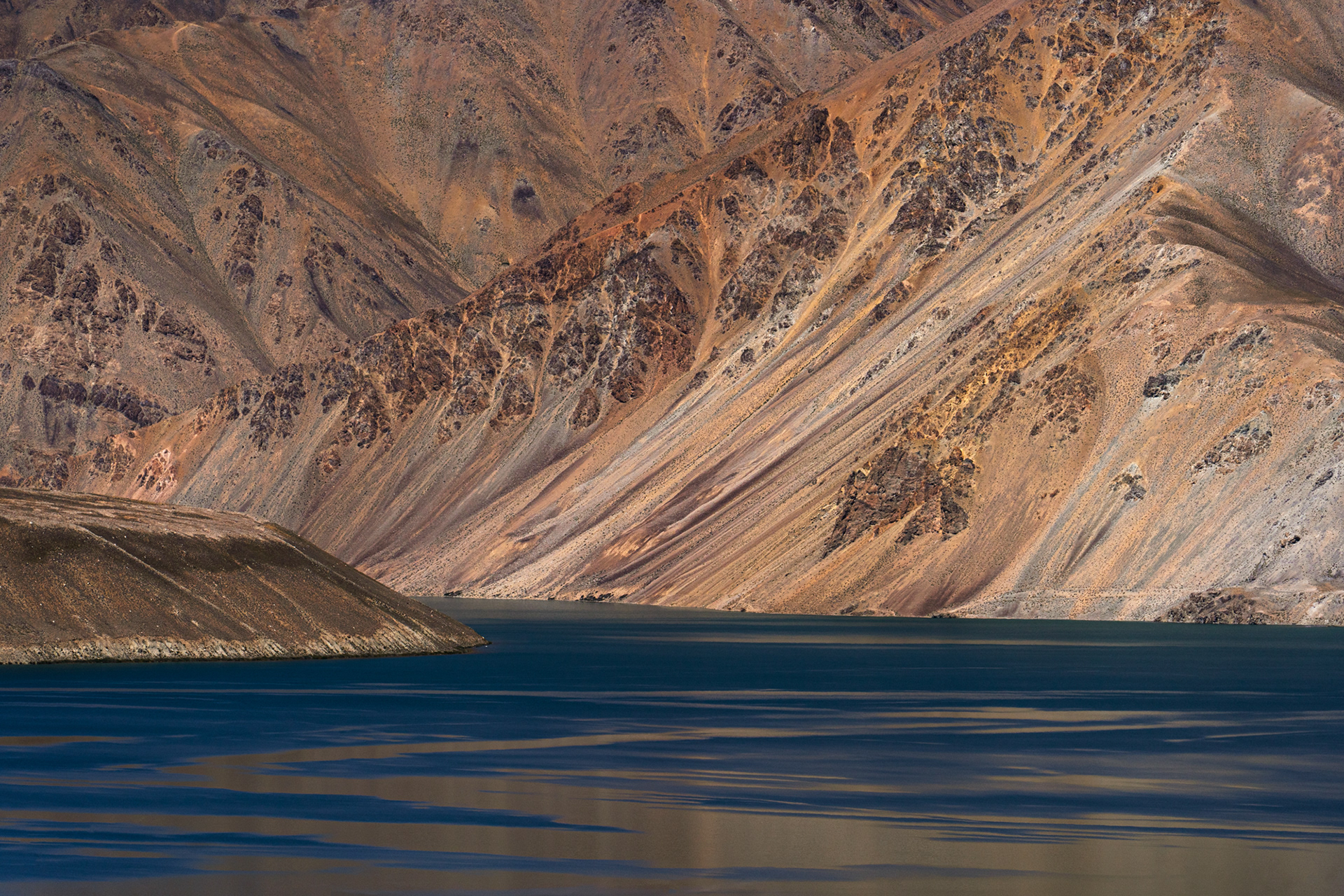 A photo of a still lake under some very textured mountains in Tajikistan.